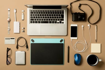 デスクに置かれたノートパソコン、カメラ、スマホ、イヤホン、タブレット、メガネ、マウス、USBなどのガジェットとアクセサリー。