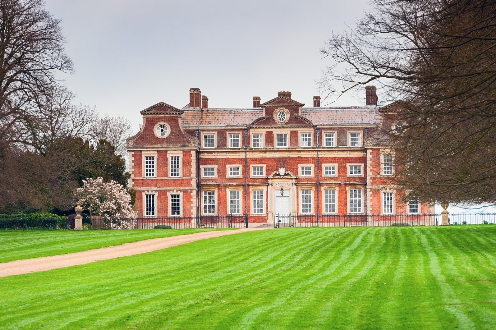 Historic mansion with aggregate chimneys, symmetrical windows, and a manicured tract surrounded by trees, conveying an elegant and timeless atmosphere