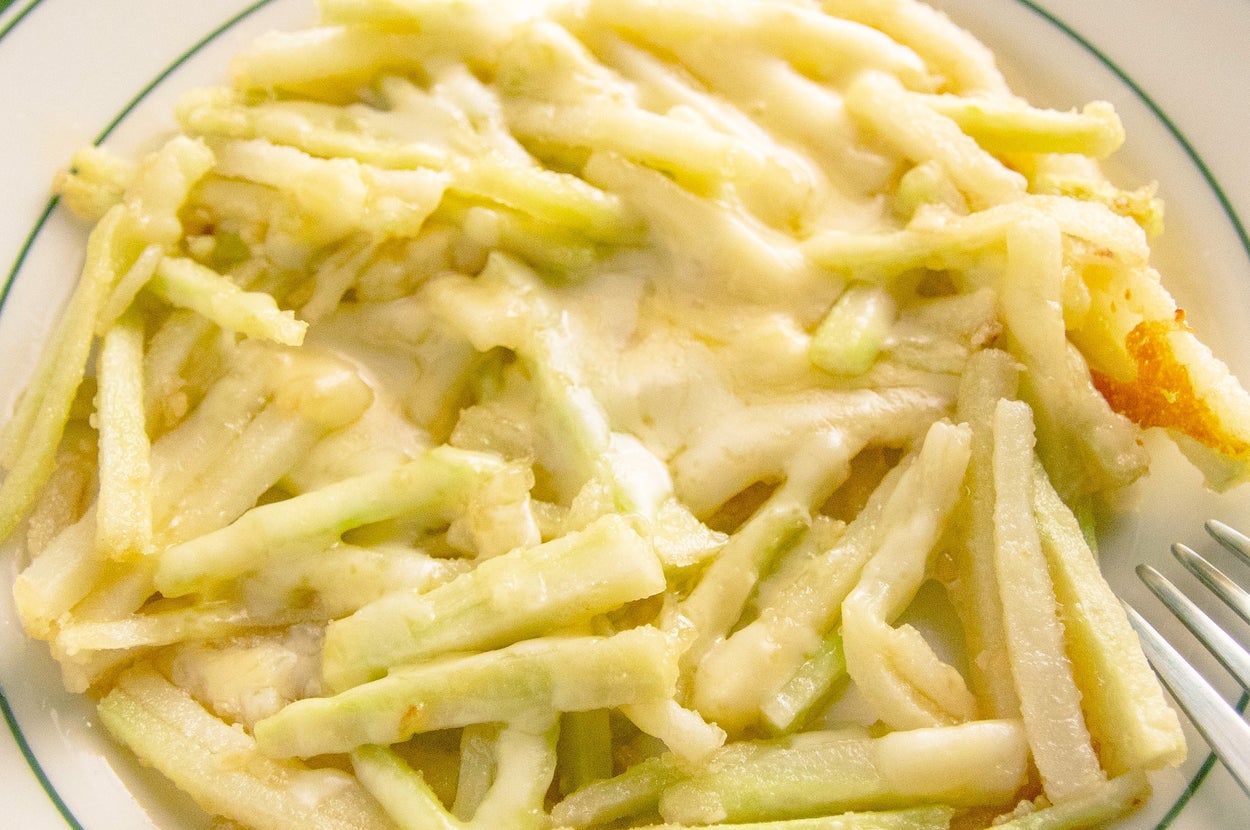 皿に盛られたチーズをかけた細切りポテト料理。フォークが添えられている。