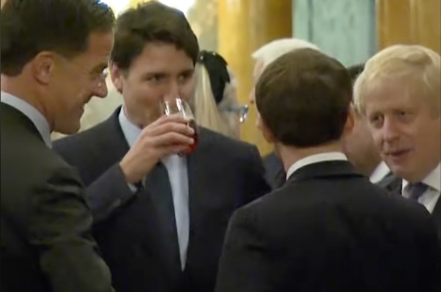 Gruppe av formelt kledde individer, engasjert i samtale ved en sosial begivenhet, med en person som nipper til en drink