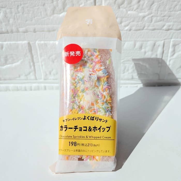 セブン-イレブンの「よくばりサンド　カラーチョコ＆ホイップ」新発売のパン。カラーチョコスプレーとホイップクリームが挟まれ、価格は198円と表示。