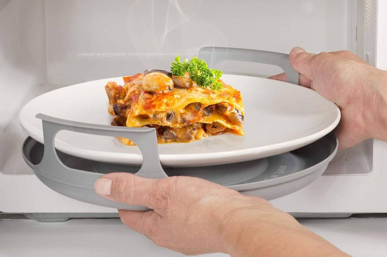 Hands placing a plate of lasagna into a microwave using a heat-resistant tray