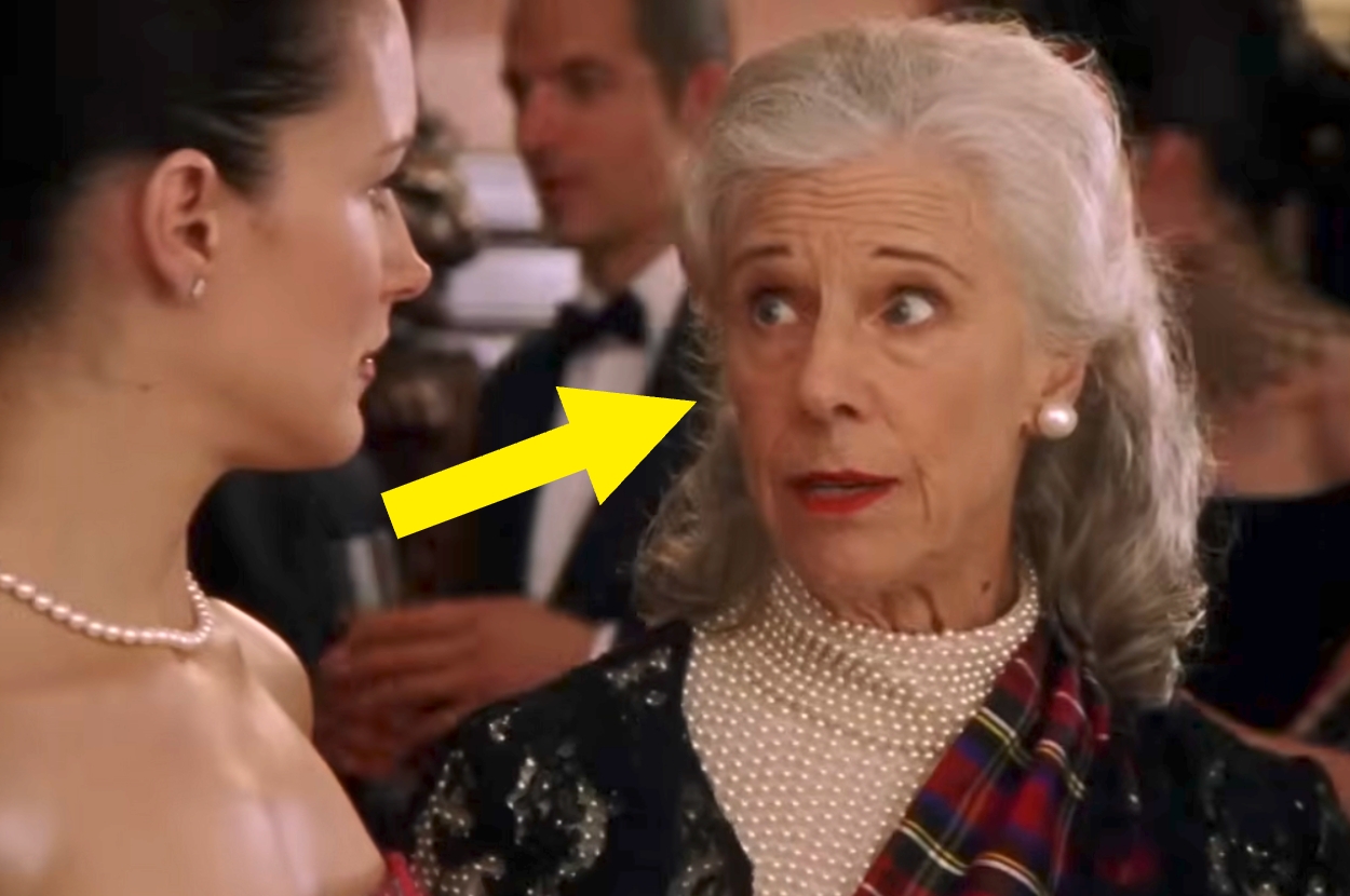 Two women at a formal event, one in pearls, the other in an elegant dress, looking at each other in surprise