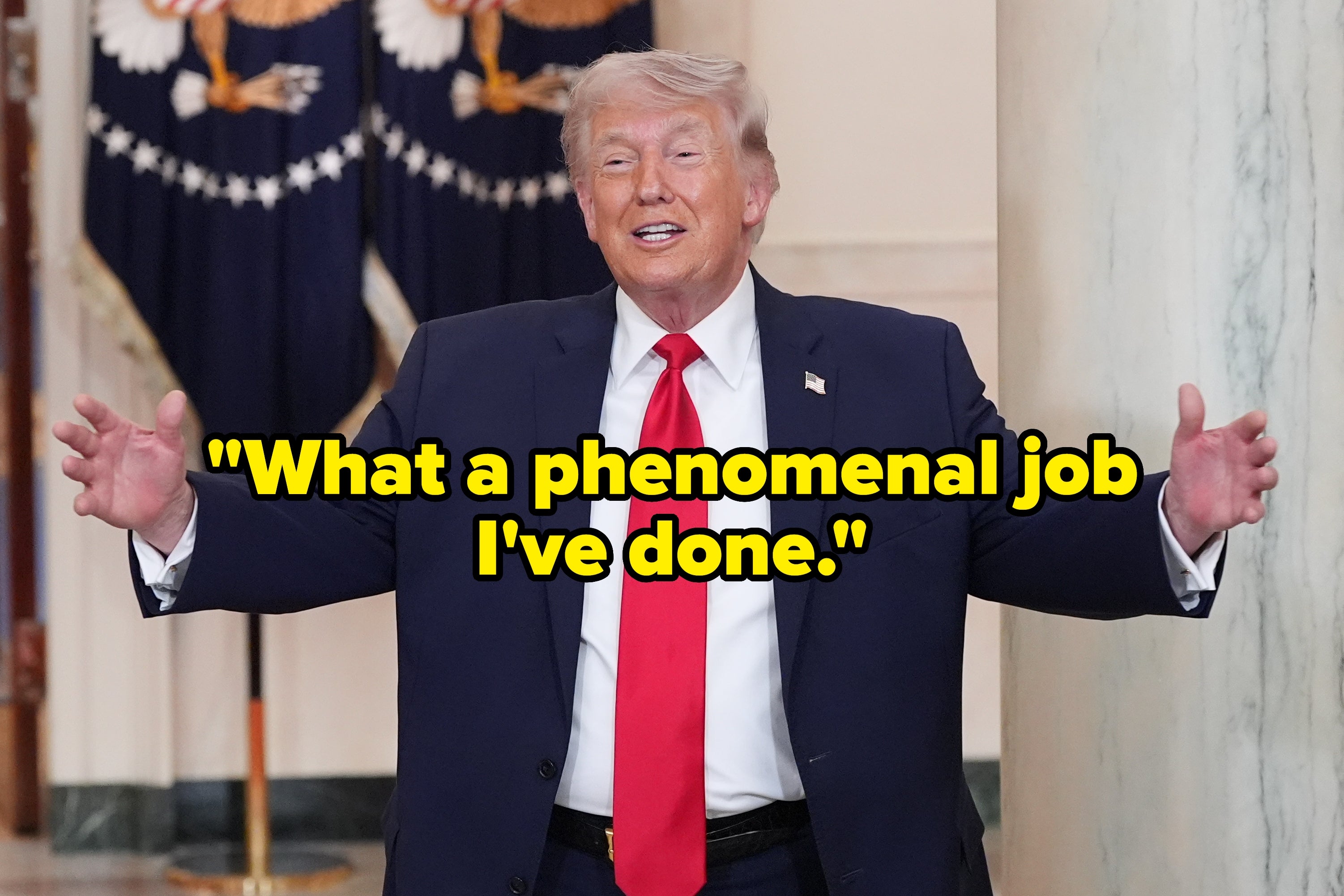 En mann i dress og rødt slips bevegelser med åpne armer inne i en formell setting med dekorative flagg i bakgrunnen