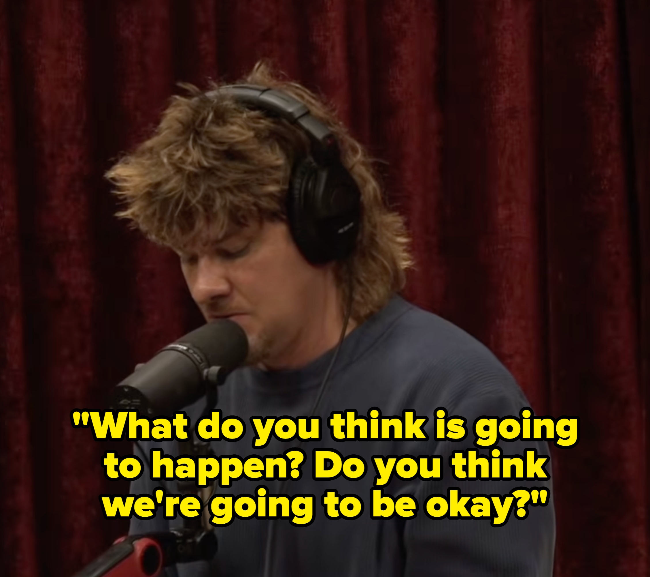 Person with headphones speaks into a microphone against a curtain backdrop, appearing focused