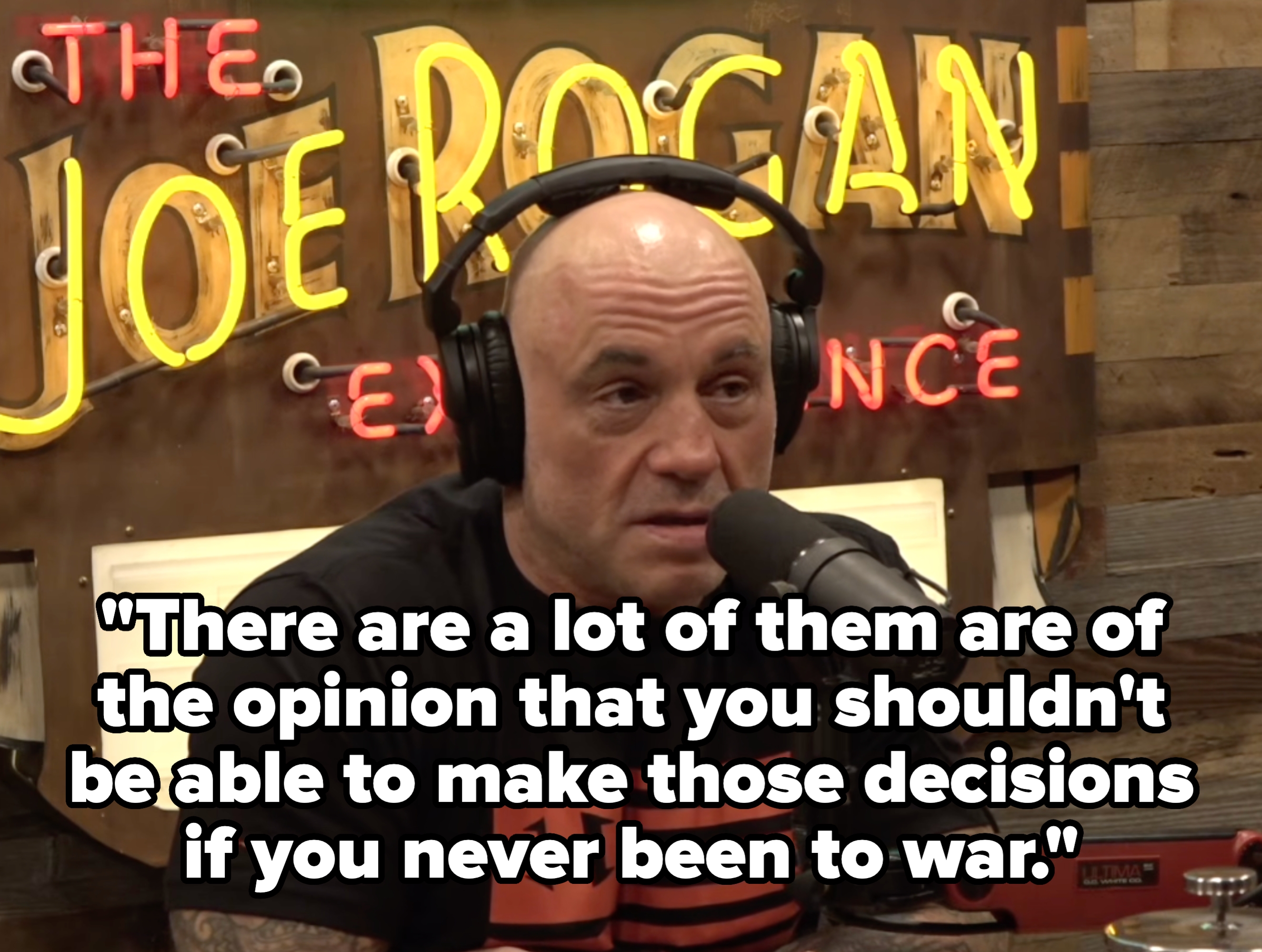 A idiosyncratic   wearing headphones and a achromatic  T-shirt speaks into a microphone successful  beforehand   of a podcast sign