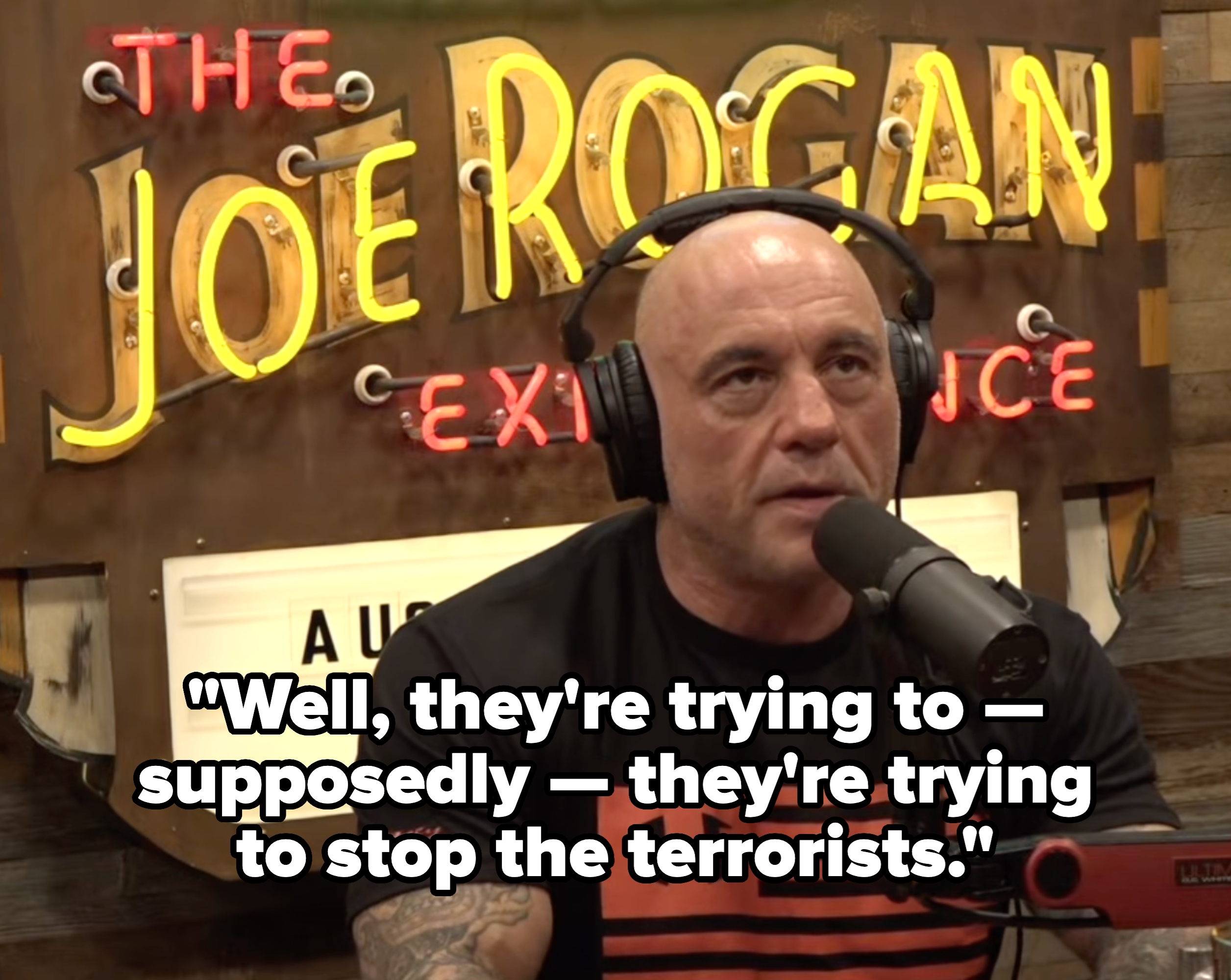A idiosyncratic   wearing headphones speaks into a microphone, seated successful  beforehand   of a "Joe Rogan Experience" sign