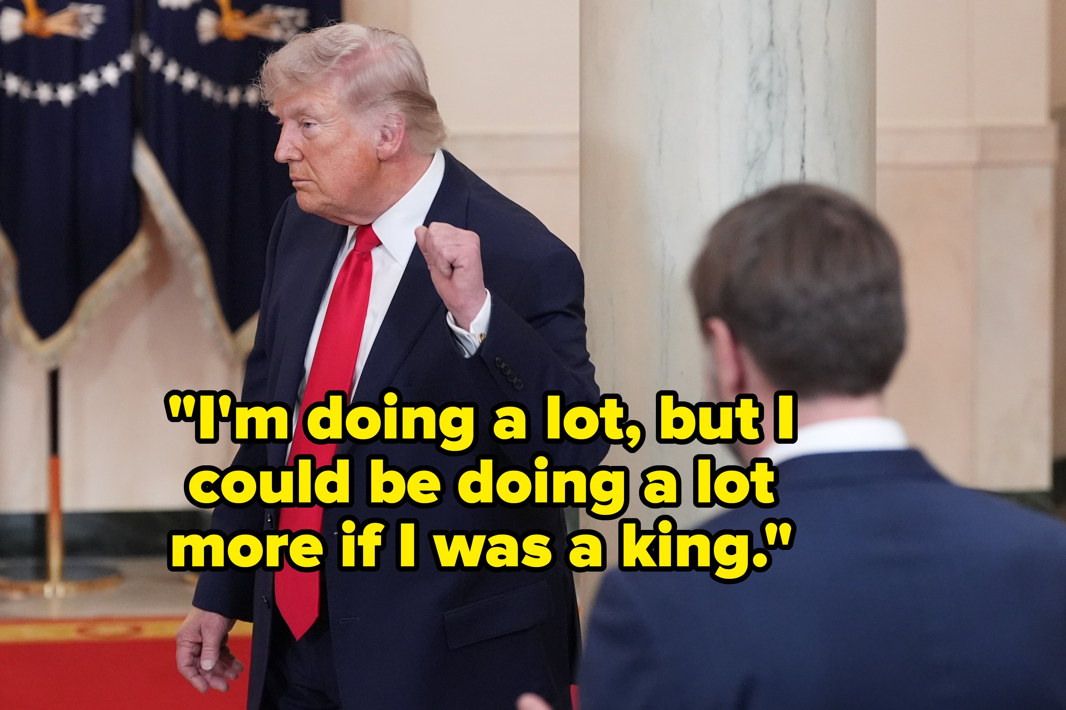 Mann i dress og rødt slips bevegelser med knyttneven; en annen person i dress er i forgrunnen. Innendørs setting med gardiner og søyle i bakgrunnen