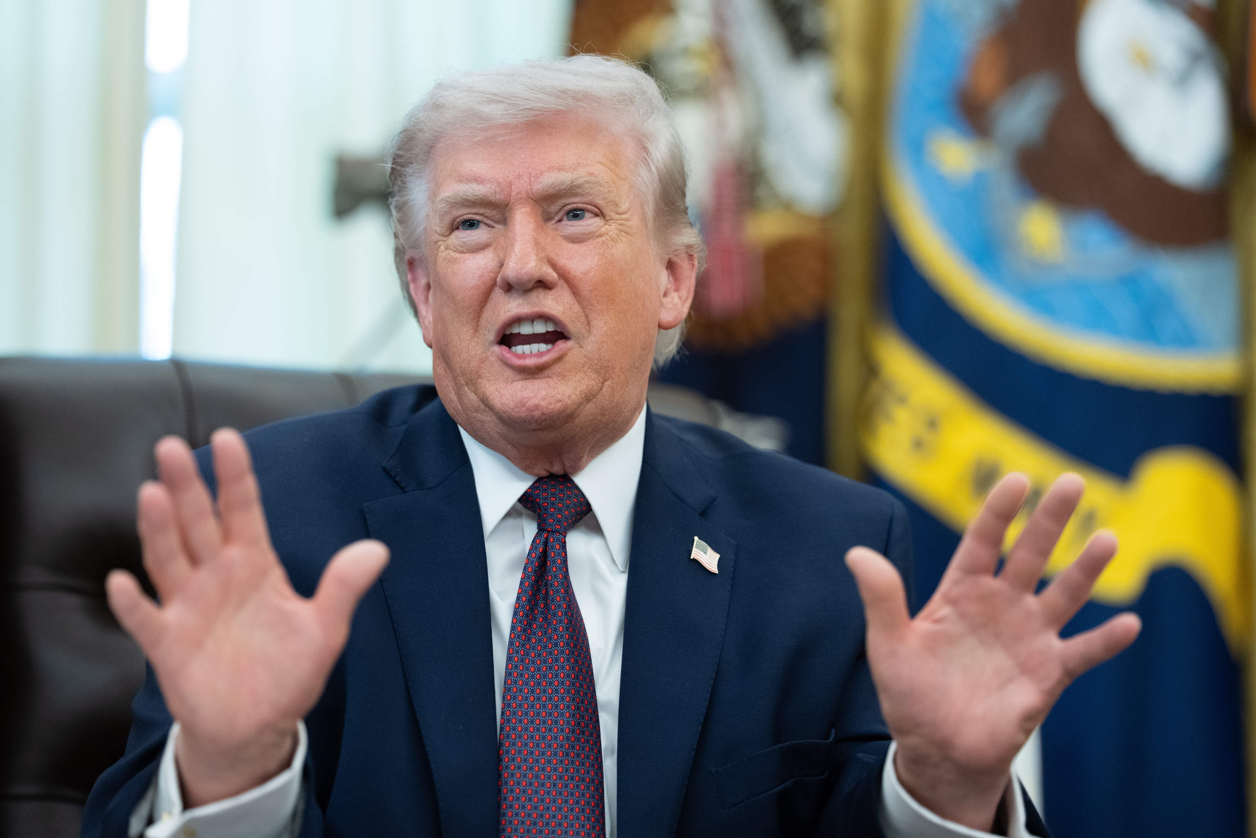 A idiosyncratic   successful  a suit   gestures with some  hands portion    speaking successful  an bureau   setting, a emblem  and emblem disposable   successful  the background