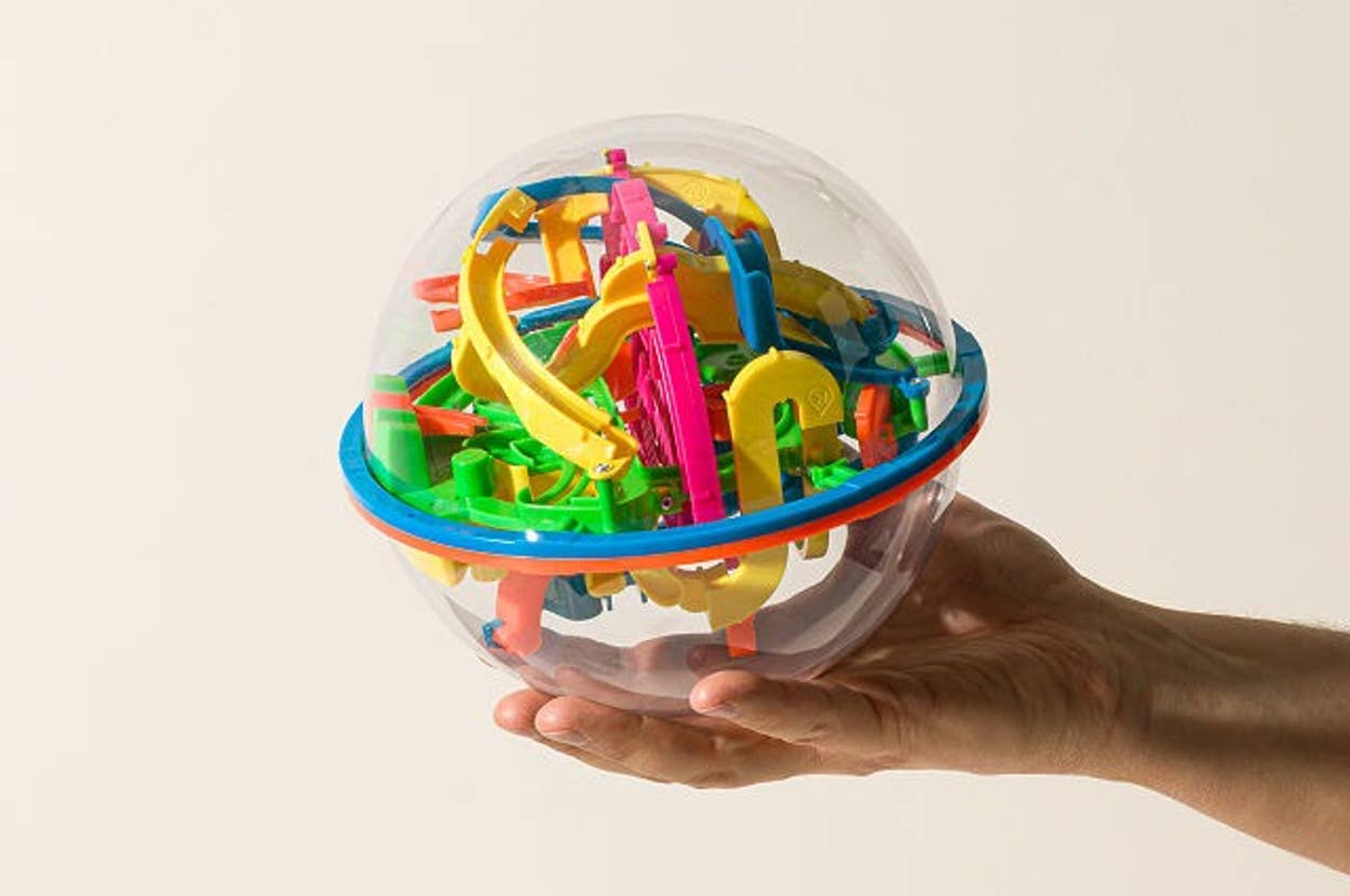 Hand holding a clear spherical toy maze with colorful pathways and obstacles