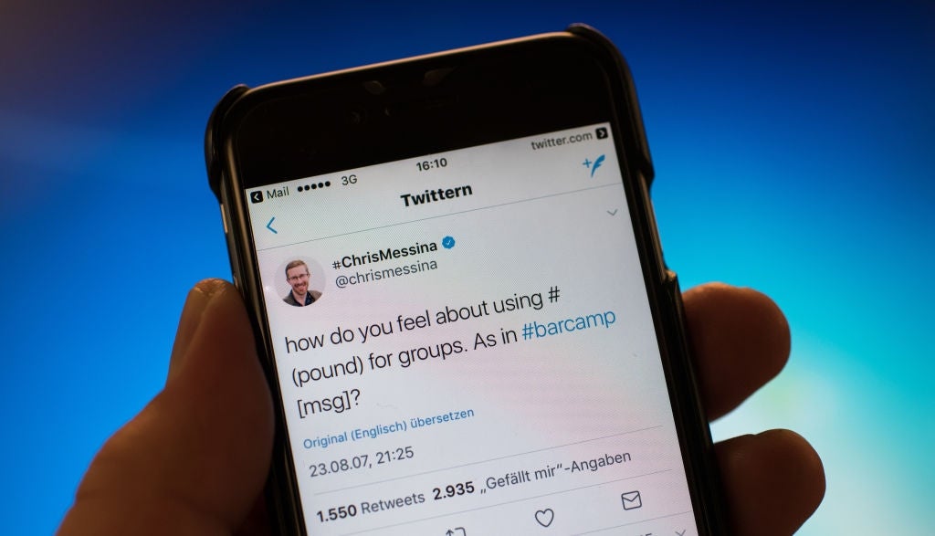 Close-up of a manus holding a telephone displaying a tweet astir utilizing the hashtag for groups, questioning its use