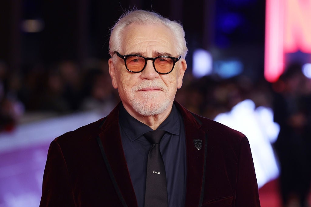 En eldre person med briller iført fløyelsdress og slips på en rød løper