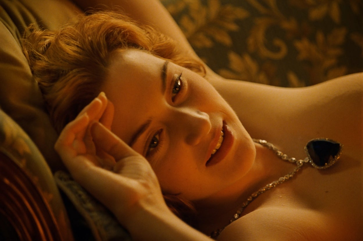Person lying on a decorative couch, wearing a necklace with a large pendant, looking to the side