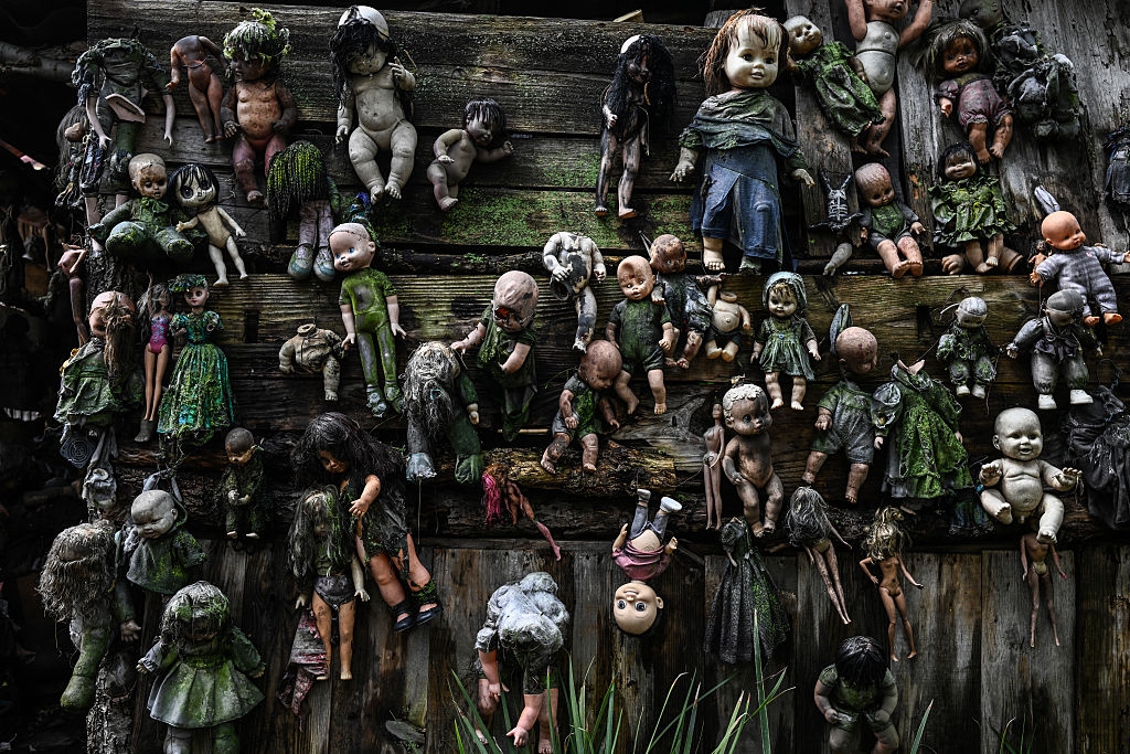Wall adorned with weathered, mud-covered dolls, creating an eerie and unsettling atmosphere