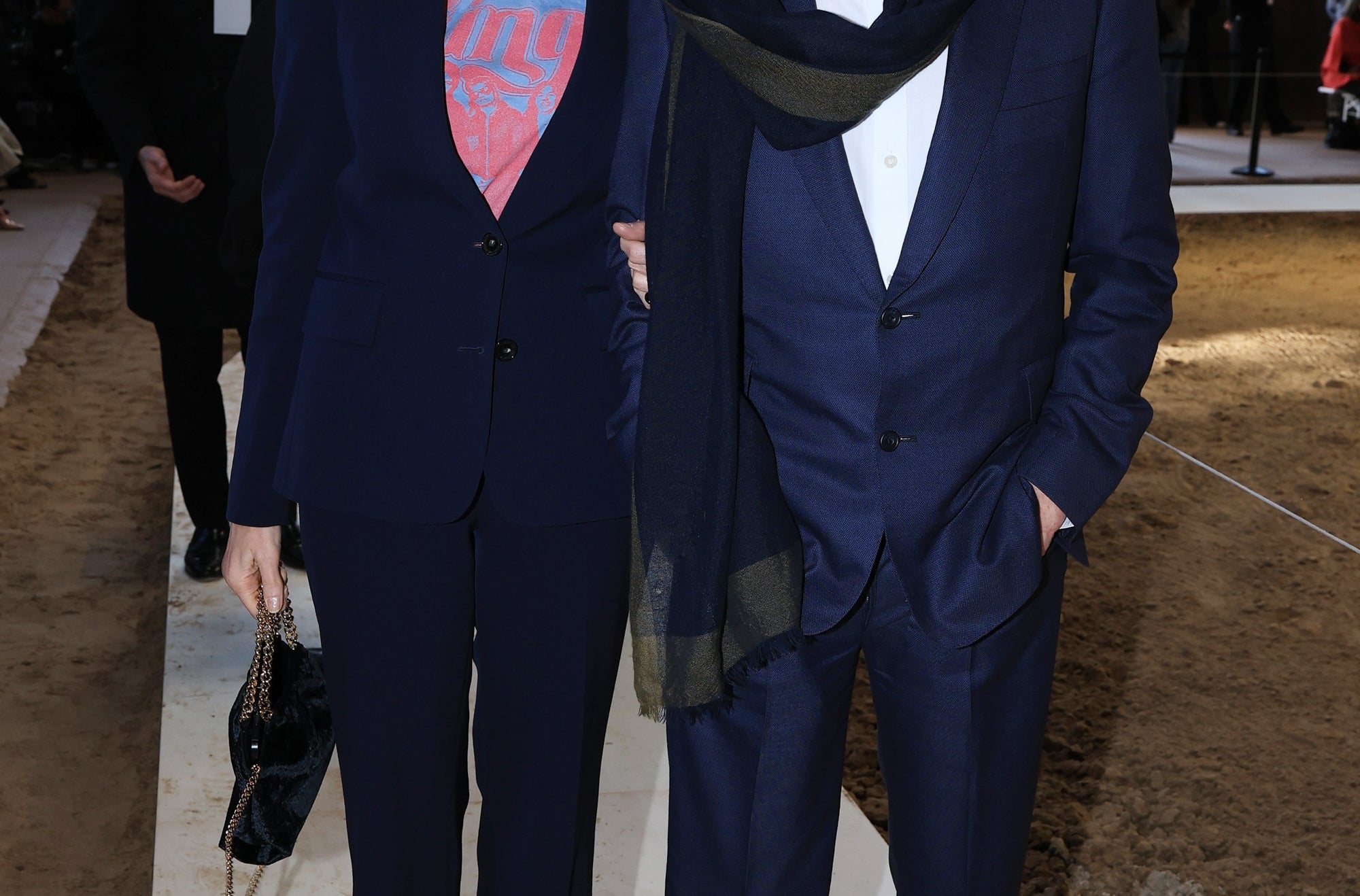 Two radical   connected  a runway. The pistillate   wears sunglasses and a stylish suit   with a graphic top. The antheral   wears a classical  suit   with a scarf