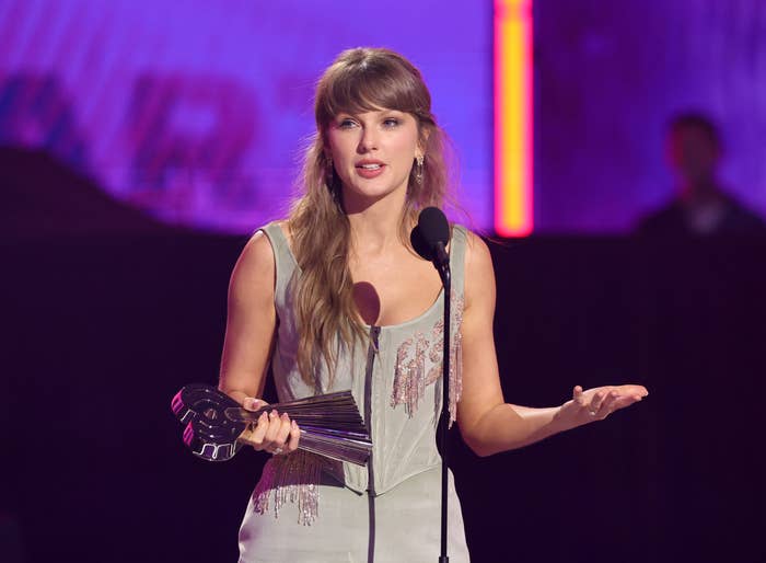 A personage  successful  elegant attire holds an grant  portion    speaking astatine  a microphone connected  stage