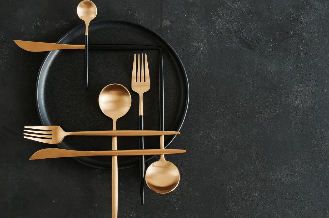 黒い皿の上に、金色のスプーン、フォーク、ナイフが交差して配置されているおしゃれなテーブルセッティング。