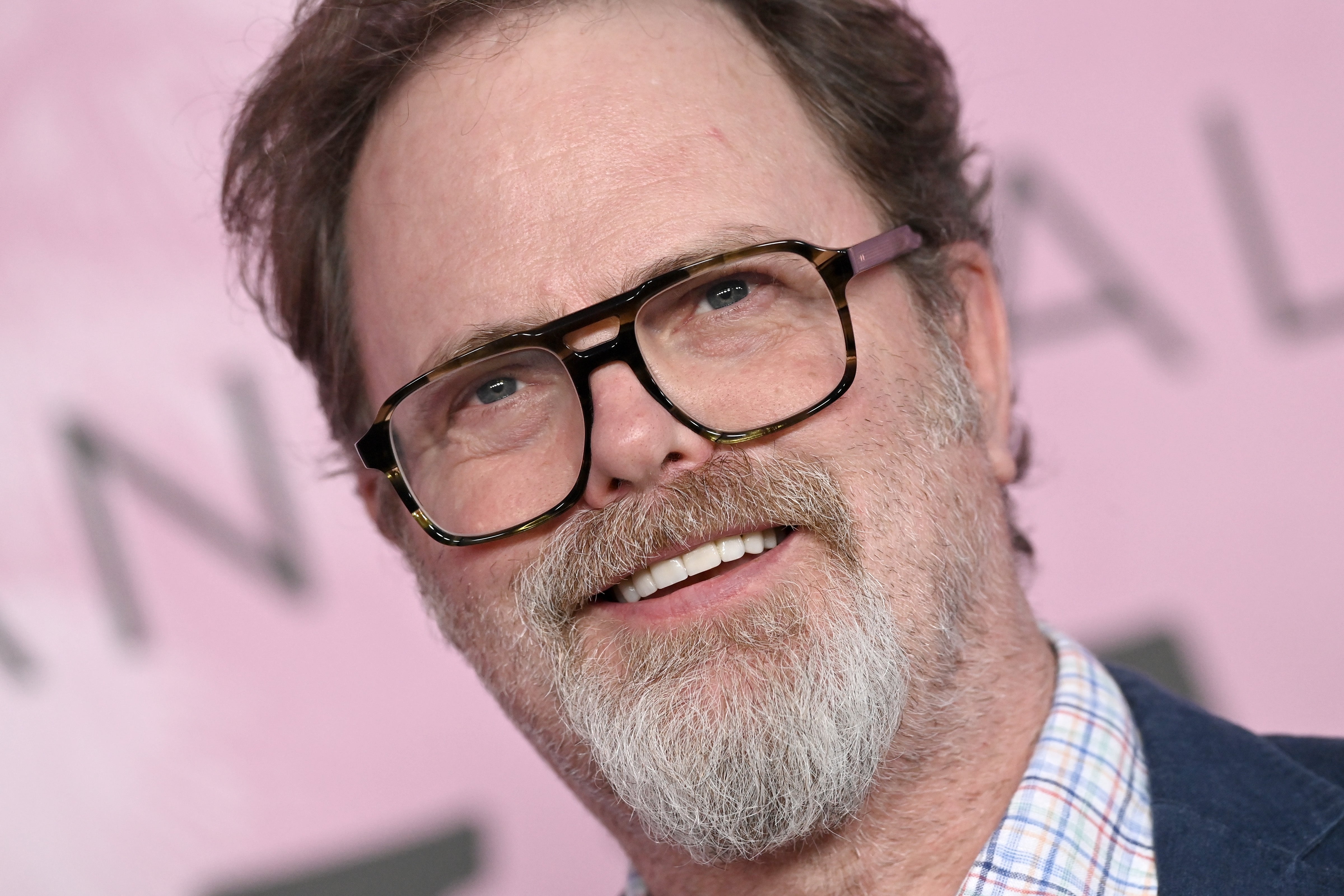 A antheral   with glasses and a beard smiles portion    wearing a checked garment  and blazer astatine  a personage  event