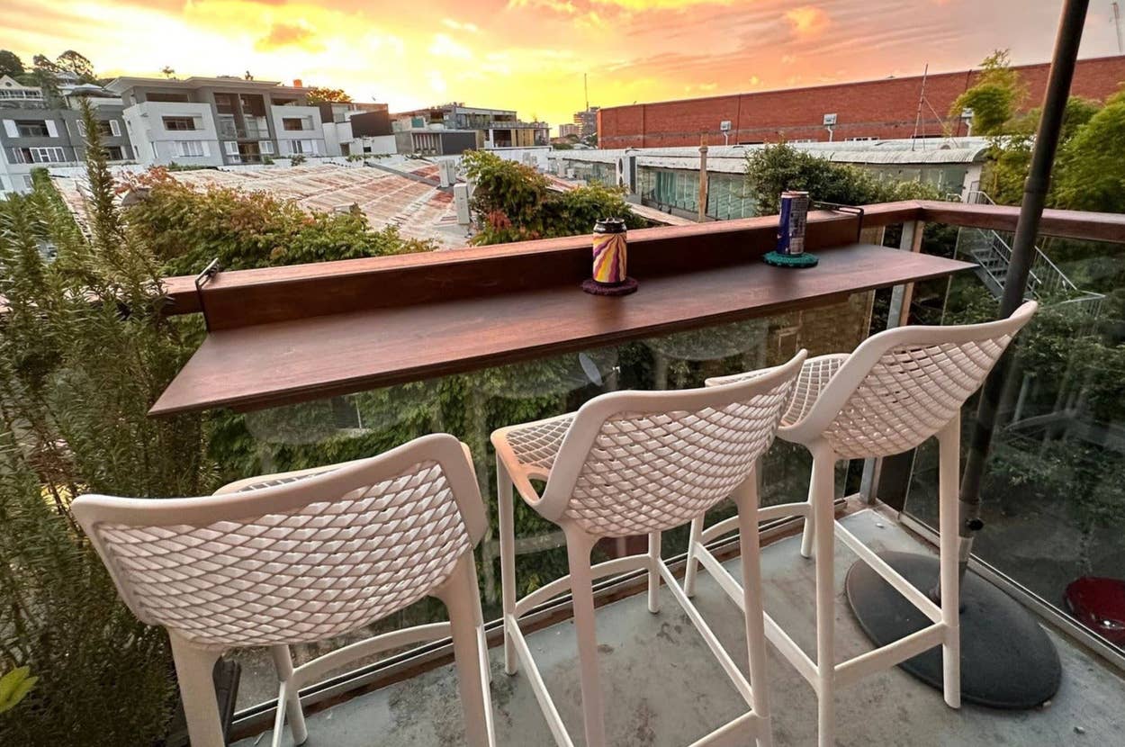 Two patterned rocking chairs with orange cushions on a porch, next to a red side table with a bouquet of red and yellow flowers