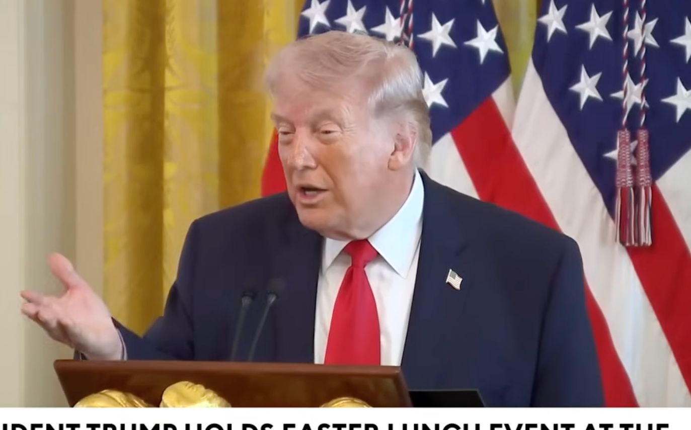 En person som taler ved et podium med amerikanske flagg i bakgrunnen, under en begivenhet i Det hvite hus, merket som 1. april 2026