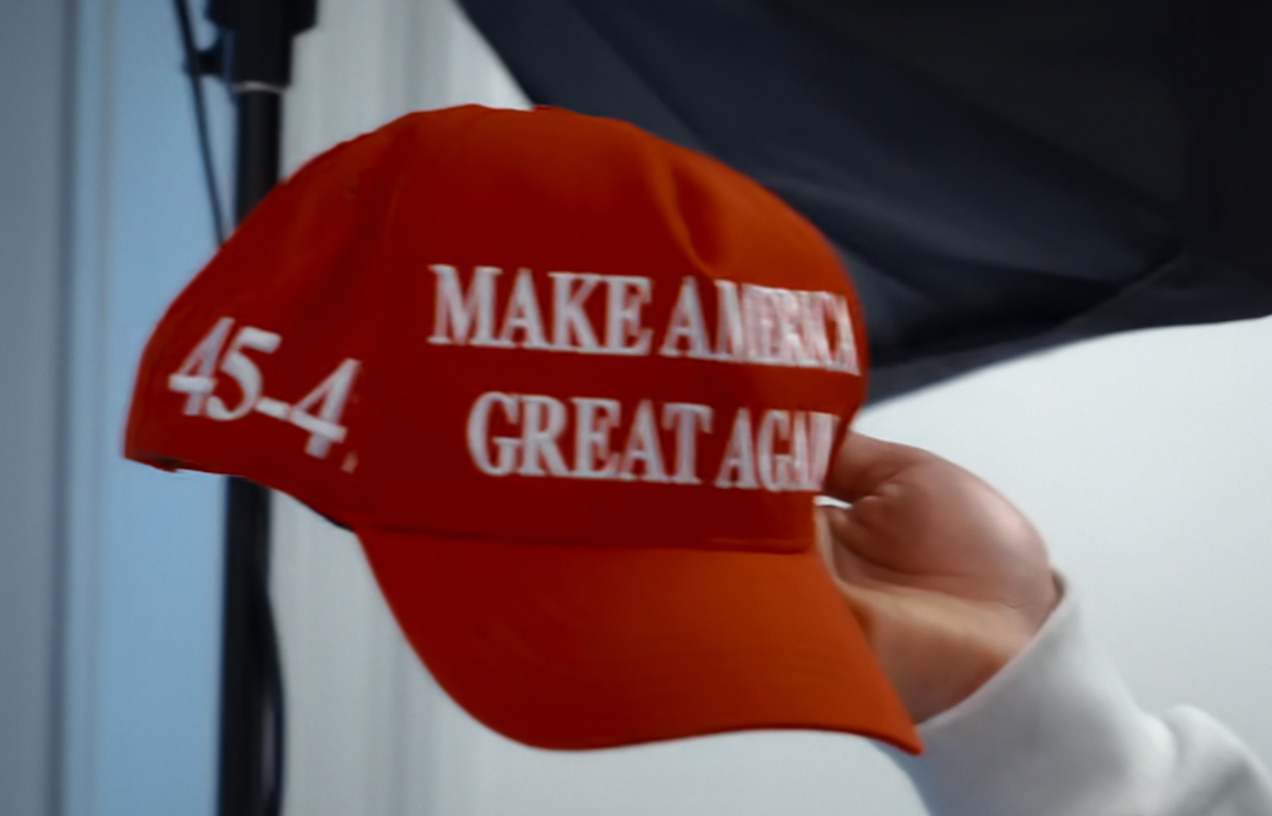 A manus holding a reddish headdress with the substance "Make America Great Again 45-4."