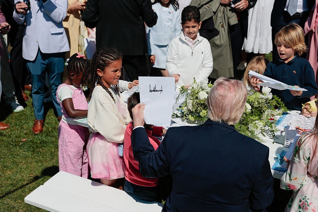 Barn samles mens en sittende mann viser dem et stykke papir under et utendørsarrangement