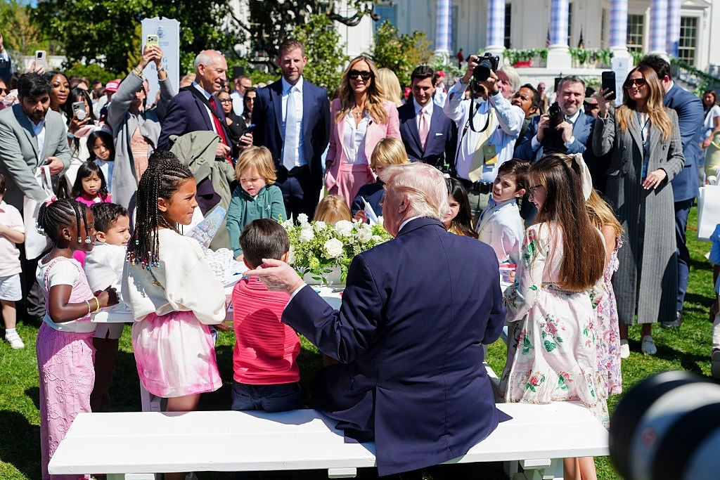 En gruppe barn og voksne, inkludert en fremtredende politisk skikkelse, samles utendørs rundt et piknikbord for et arrangement med media tilstede