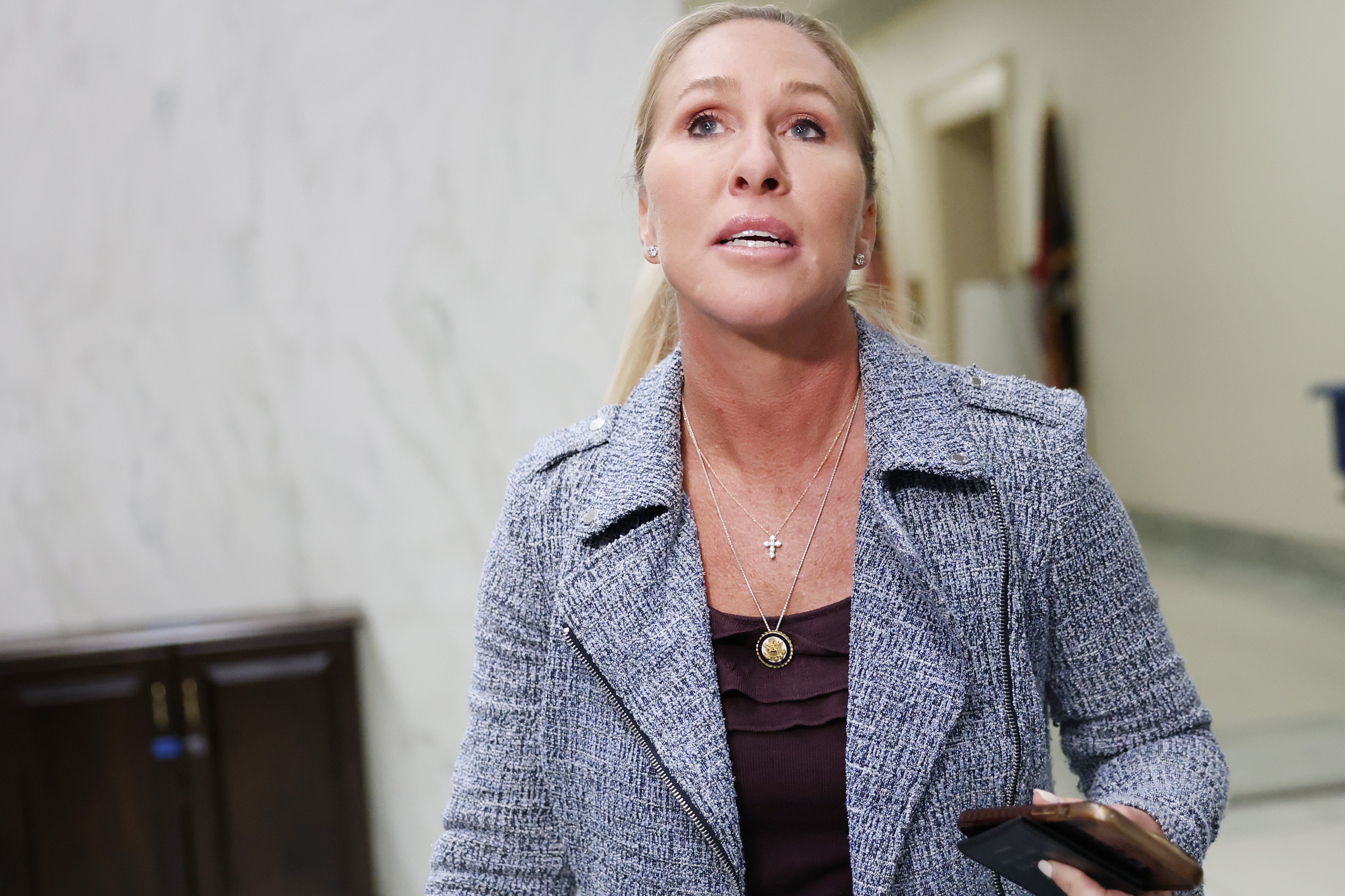 En kvinne i en teksturert blazer holder en telefon og ser ut til å snakke og stå innendørs