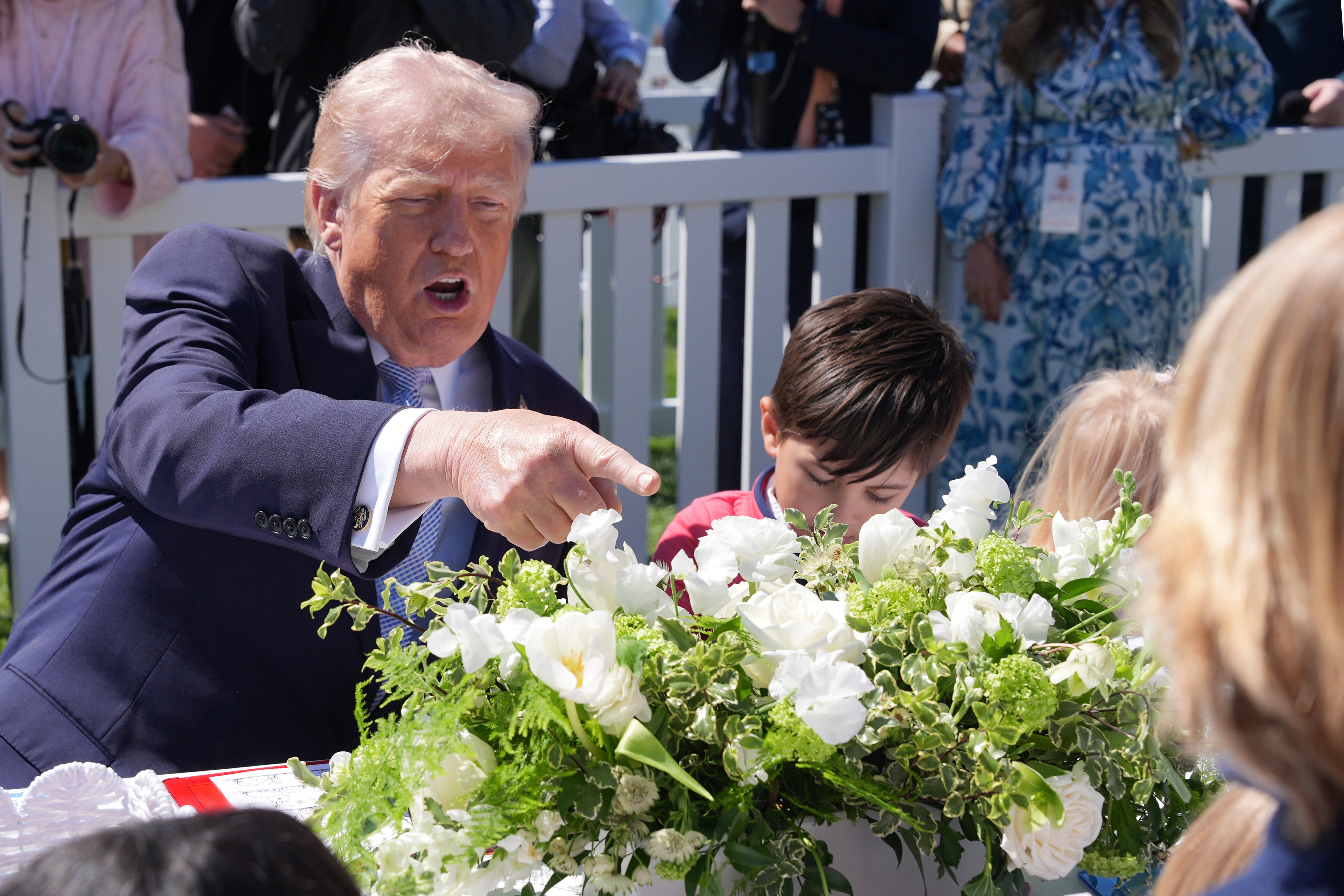 En mann i dress samhandler med barn over et bord med blomster i en festlig utesetting