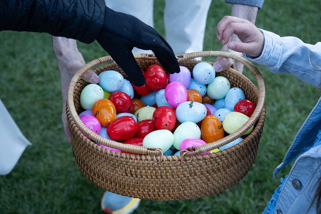 Hender som strekker seg etter en kurv fylt med fargerike påskeegg, holdt av en voksen