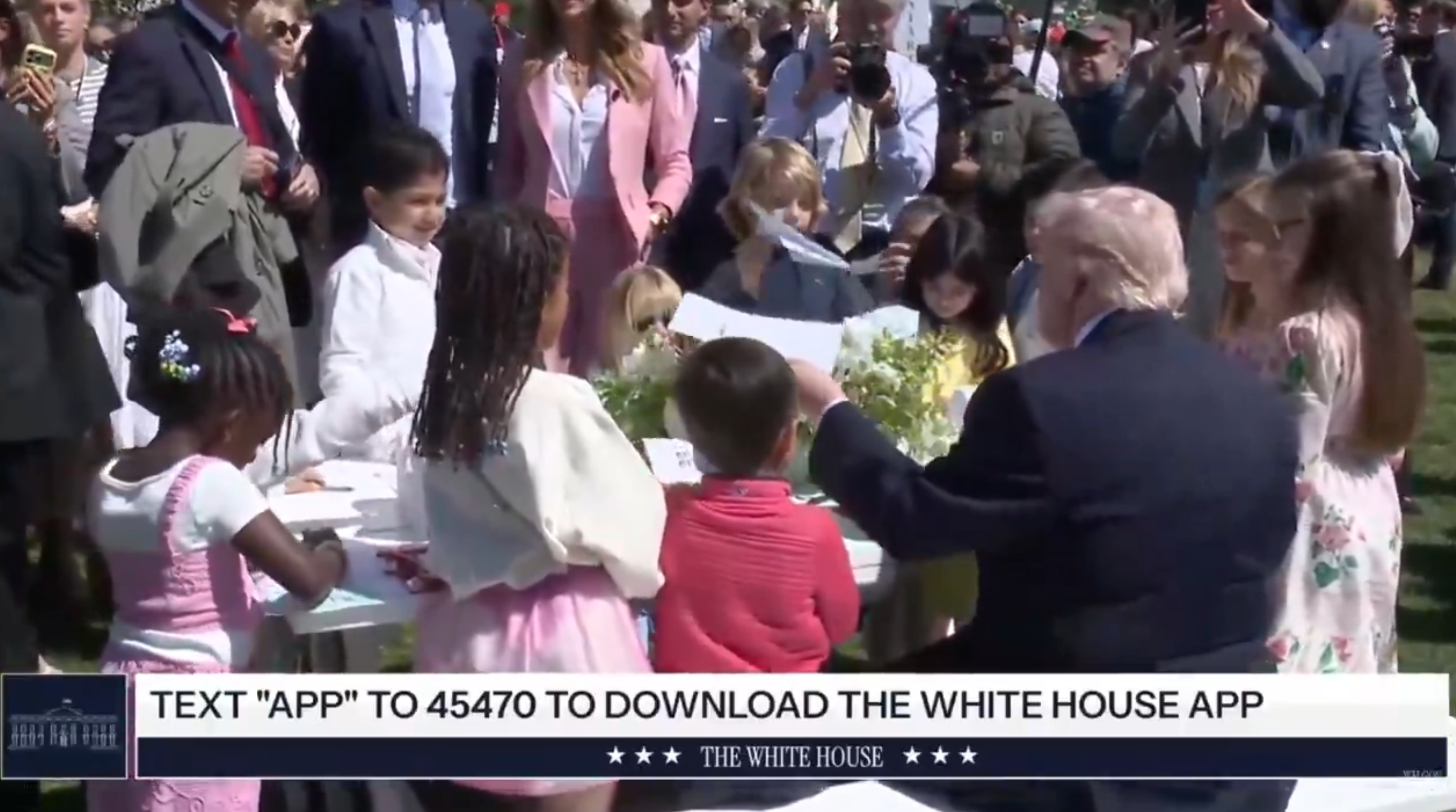 Barn deltar i et utendørsarrangement med en eldste som veileder dem. Tekst: "Tekst 'APP' til 45470 for å laste ned The White House-appen."