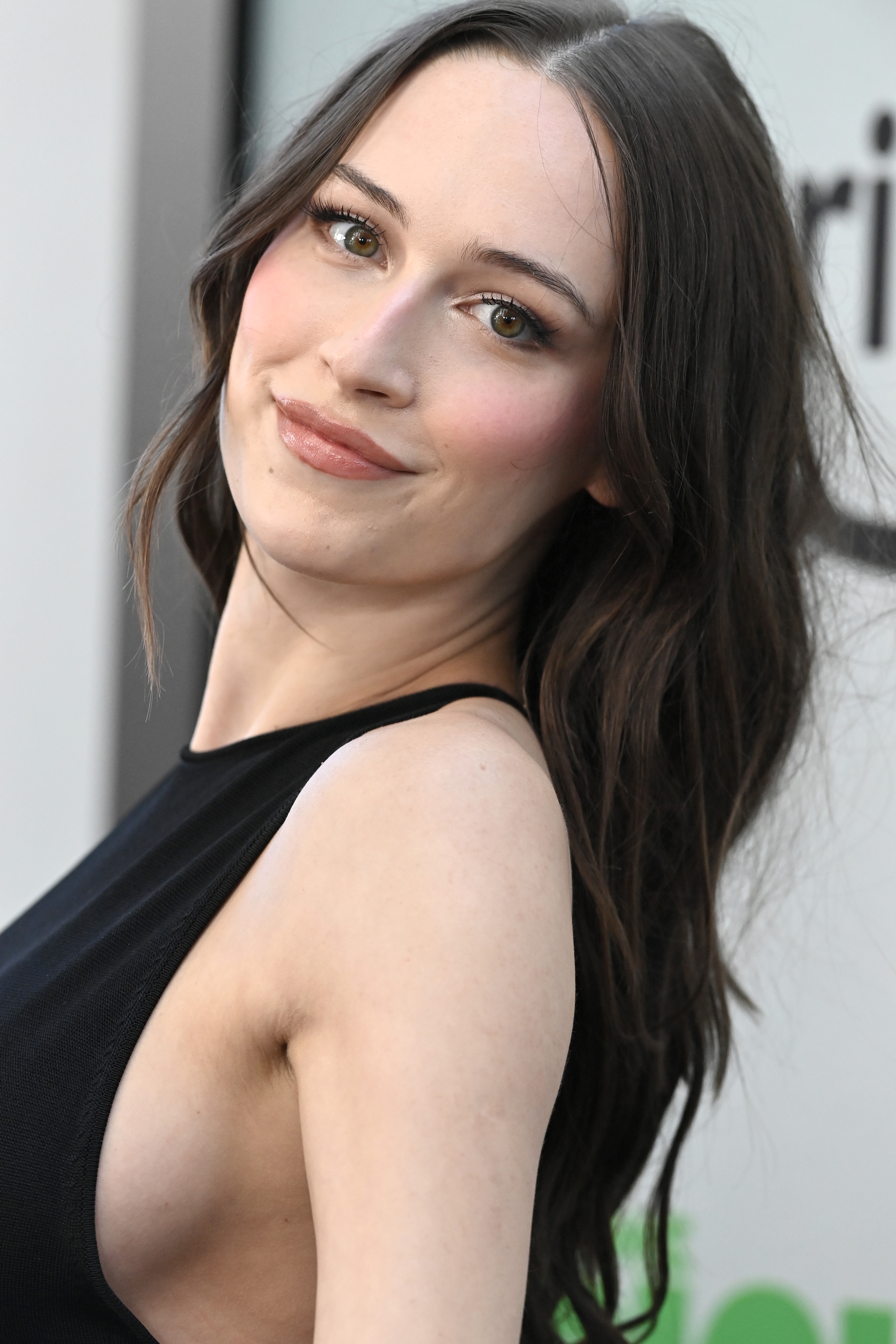 Smiling pistillate   successful  a sleeveless achromatic  dress, agelong  wavy hair, connected  a personage  lawsuit   reddish  carpet