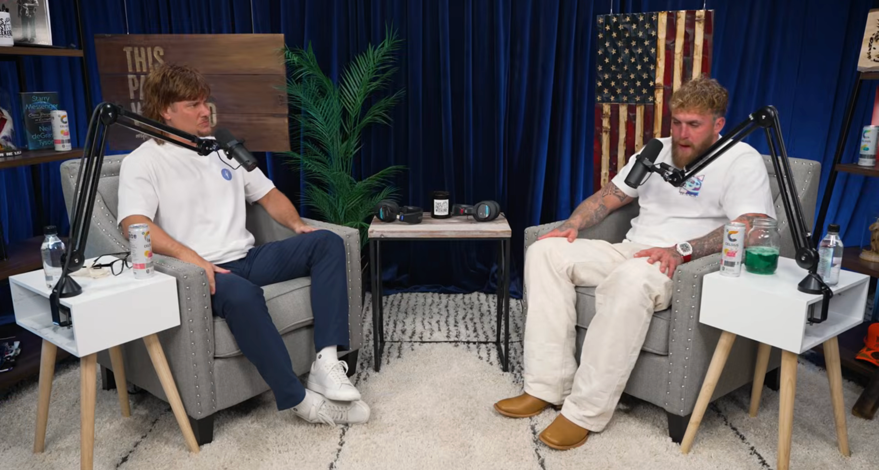 To menn sitter i et podcaststudio og snakker med mikrofoner, omgitt av dekor som et amerikansk flagg og planter