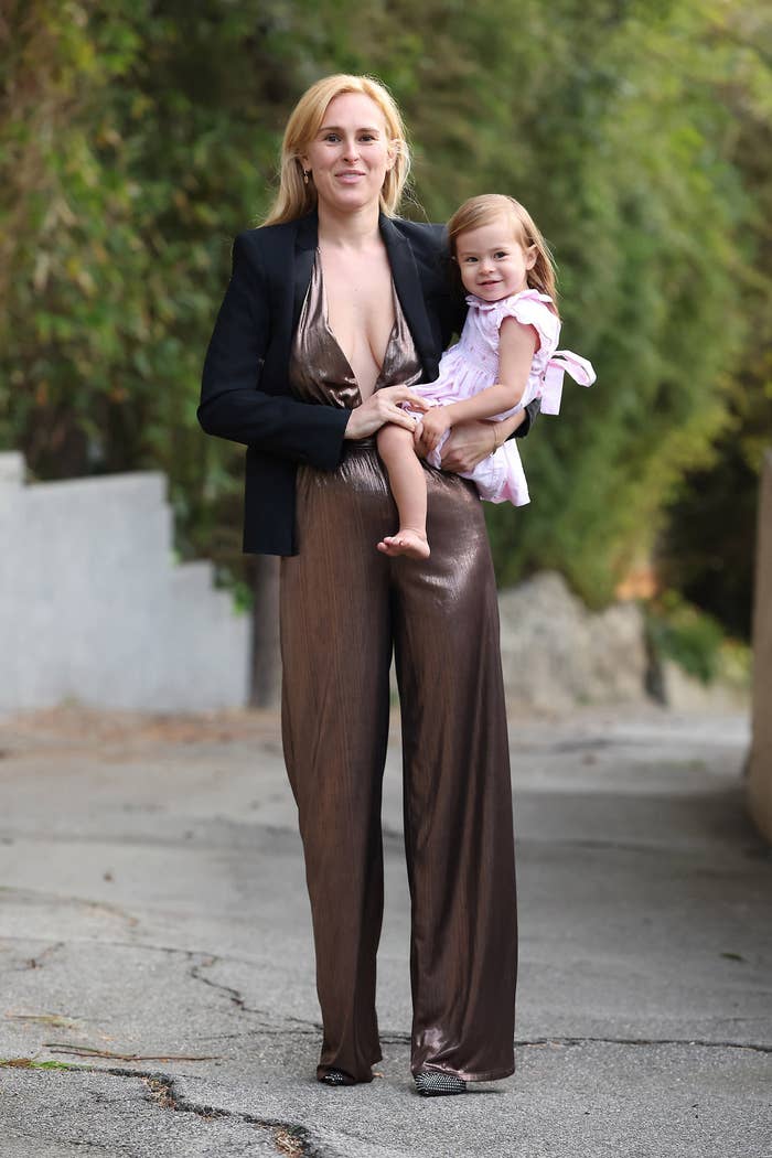 Woman successful  a sleek jumpsuit holding a young miss  successful  a dress, walking connected  a path