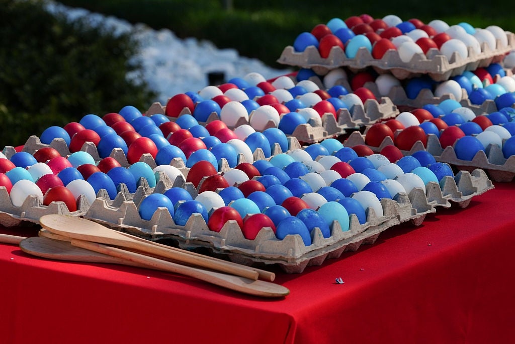 Brett med fargede egg i forskjellige farger vises på en rød duk, med treskjeer ved siden av dem