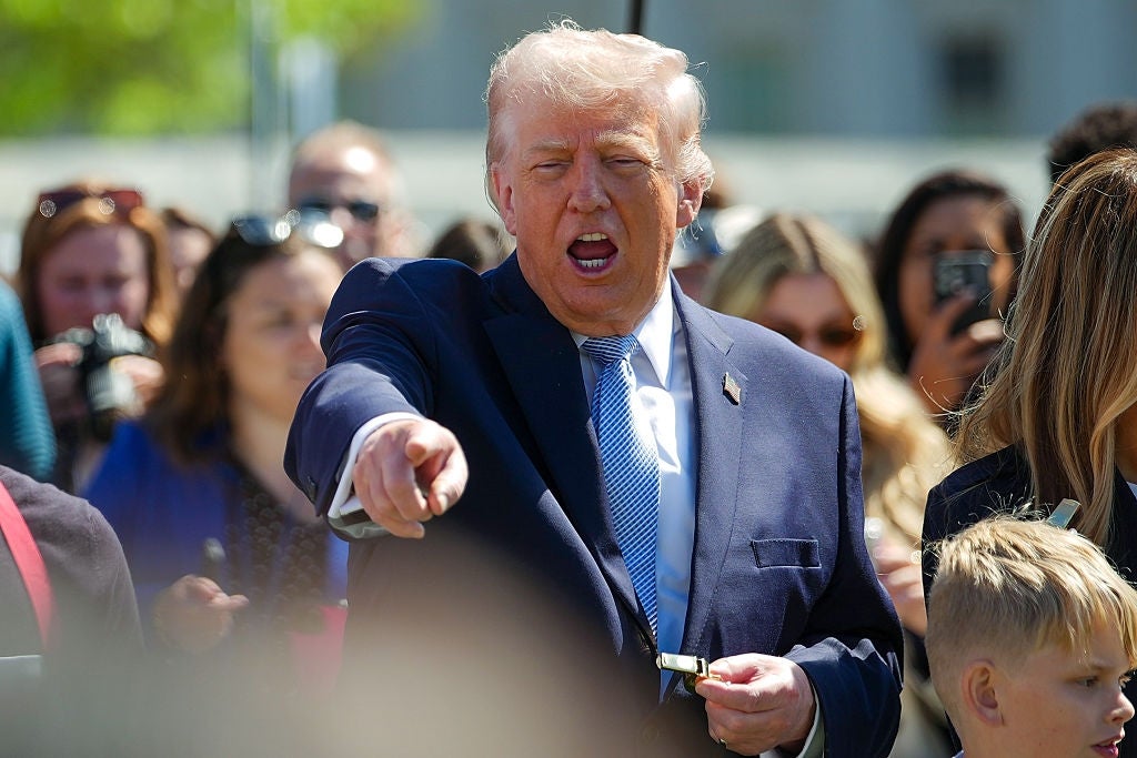 En mann i dress peker og snakker animert på et utendørsarrangement, omgitt av en mengde tilskuere