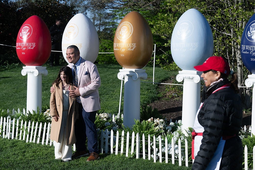 Mann og kvinne poserer lykkelig foran store dekorative egg på et offentlig arrangement med en annen person i forgrunnen
