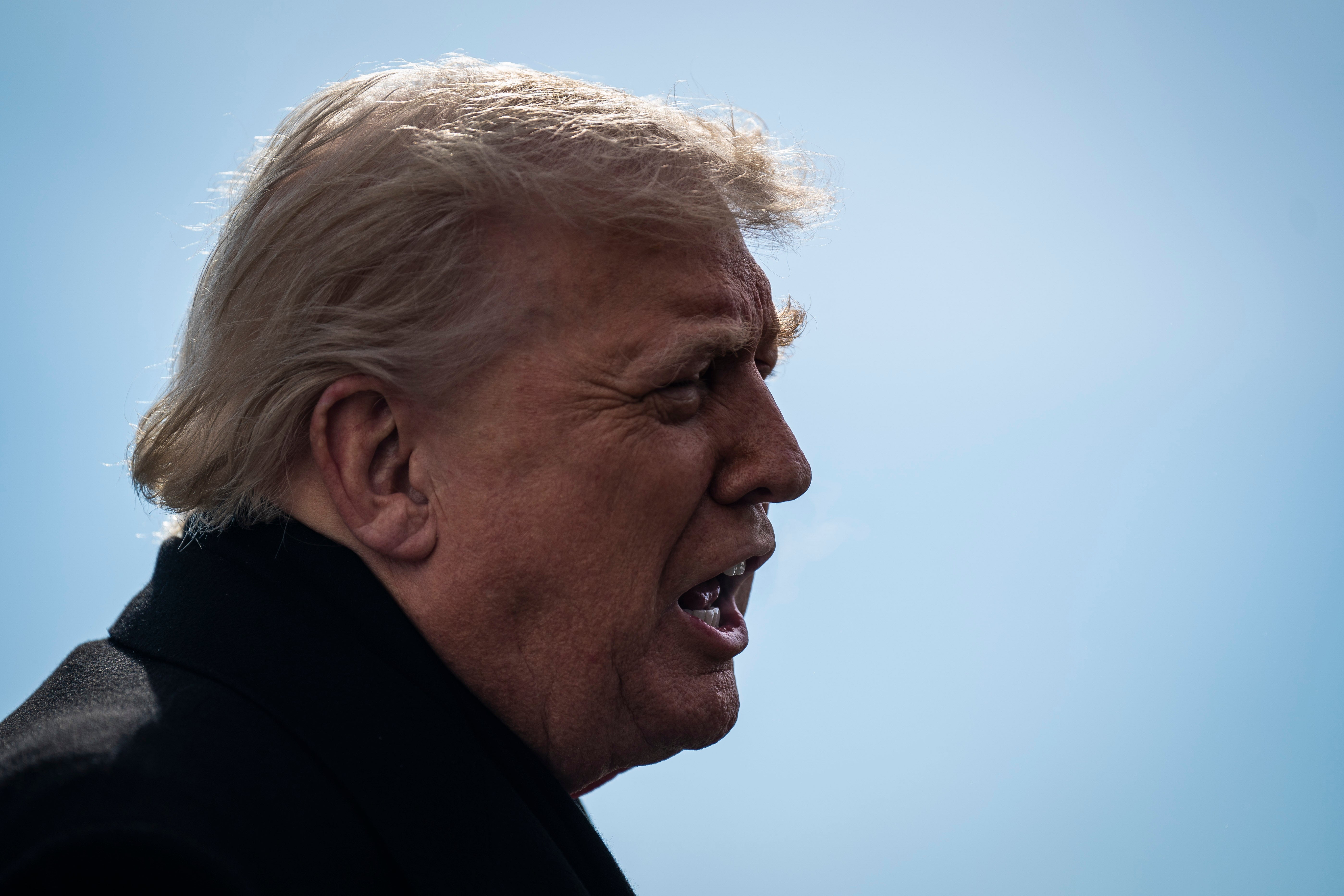 En person i profil med vindblåst hår snakker utendørs mot en klar himmel som bakteppe