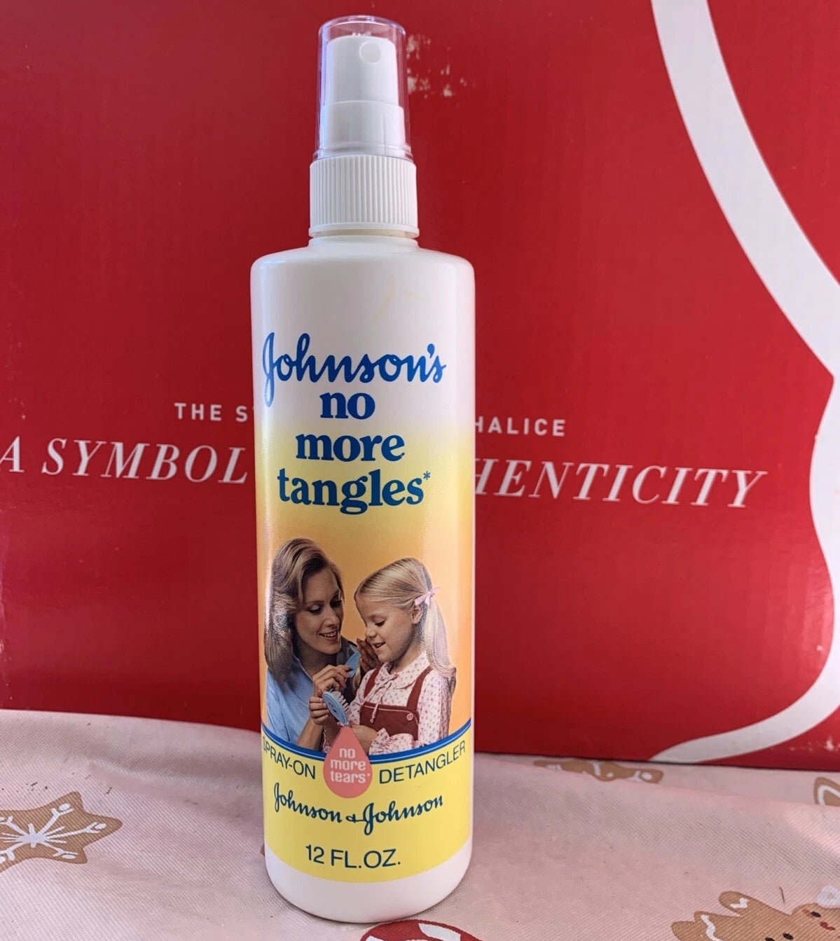 Bottle of Johnson's No More Tangles spray with statement featuring parent and child. Background has partially disposable substance and design