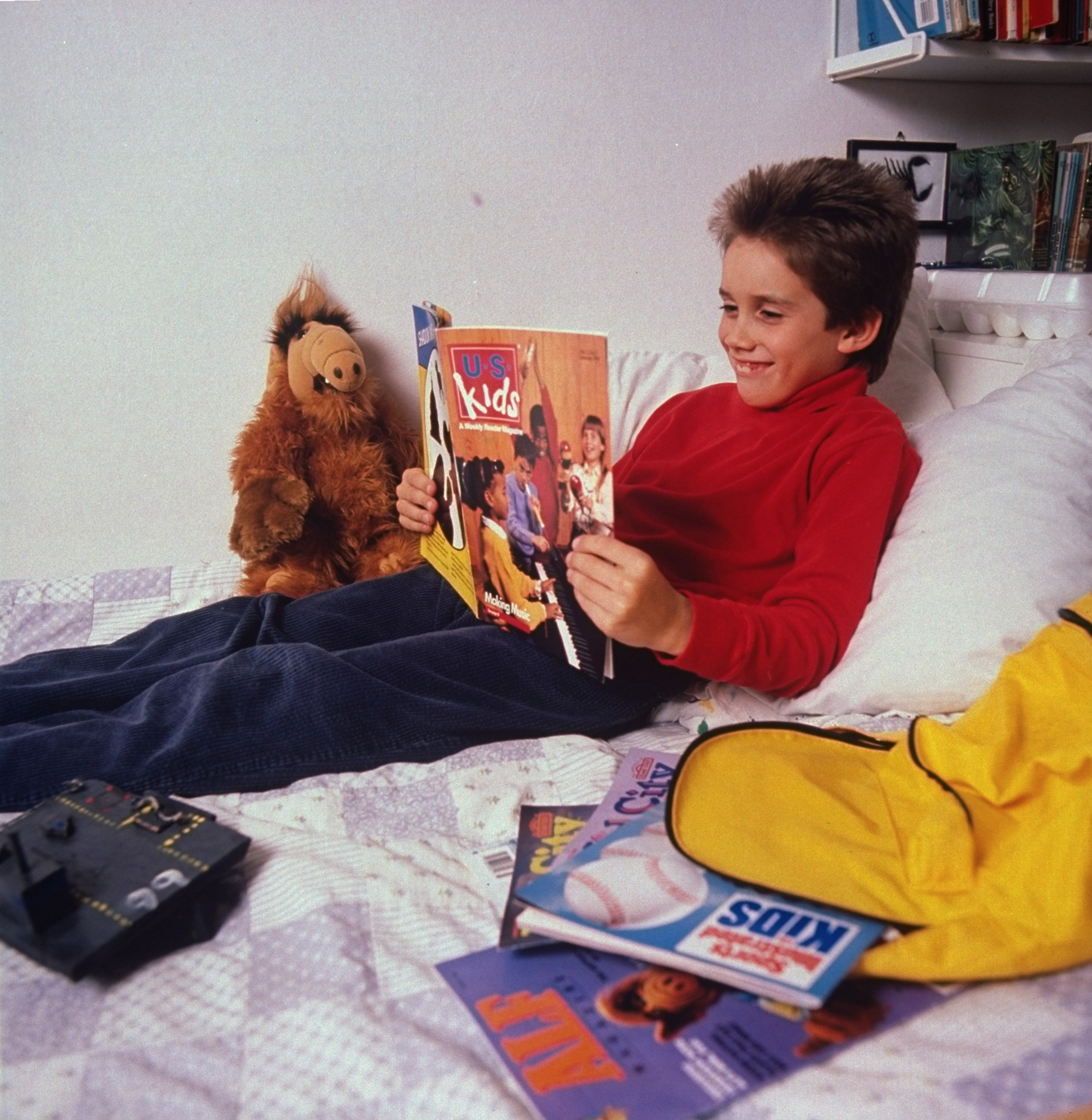 Child speechmaking a "Kids" mag connected a bed, surrounded by much magazines and a plush toy, creating a nostalgic 80s chamber scene