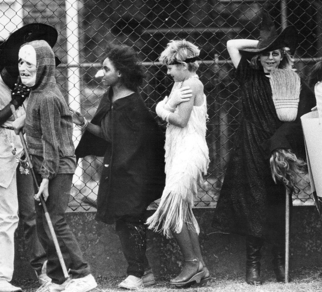 Children successful Halloween costumes, including a ghoul, witch, and flapper, lined up successful beforehand of a fence, participating successful a festive event