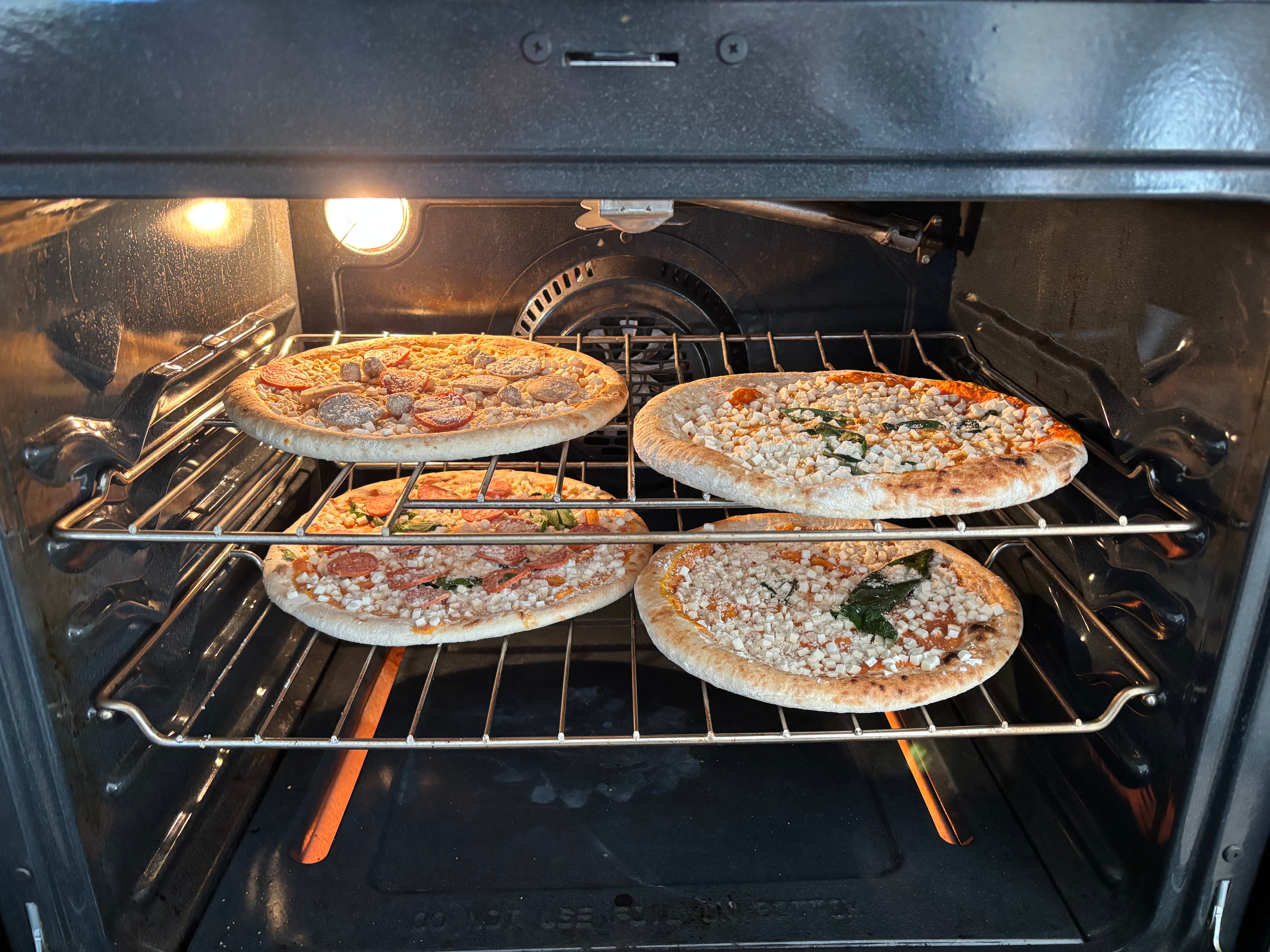 Four pizzas baking in an oven, with toppings like cheese, spinach, and pepperoni visible on some