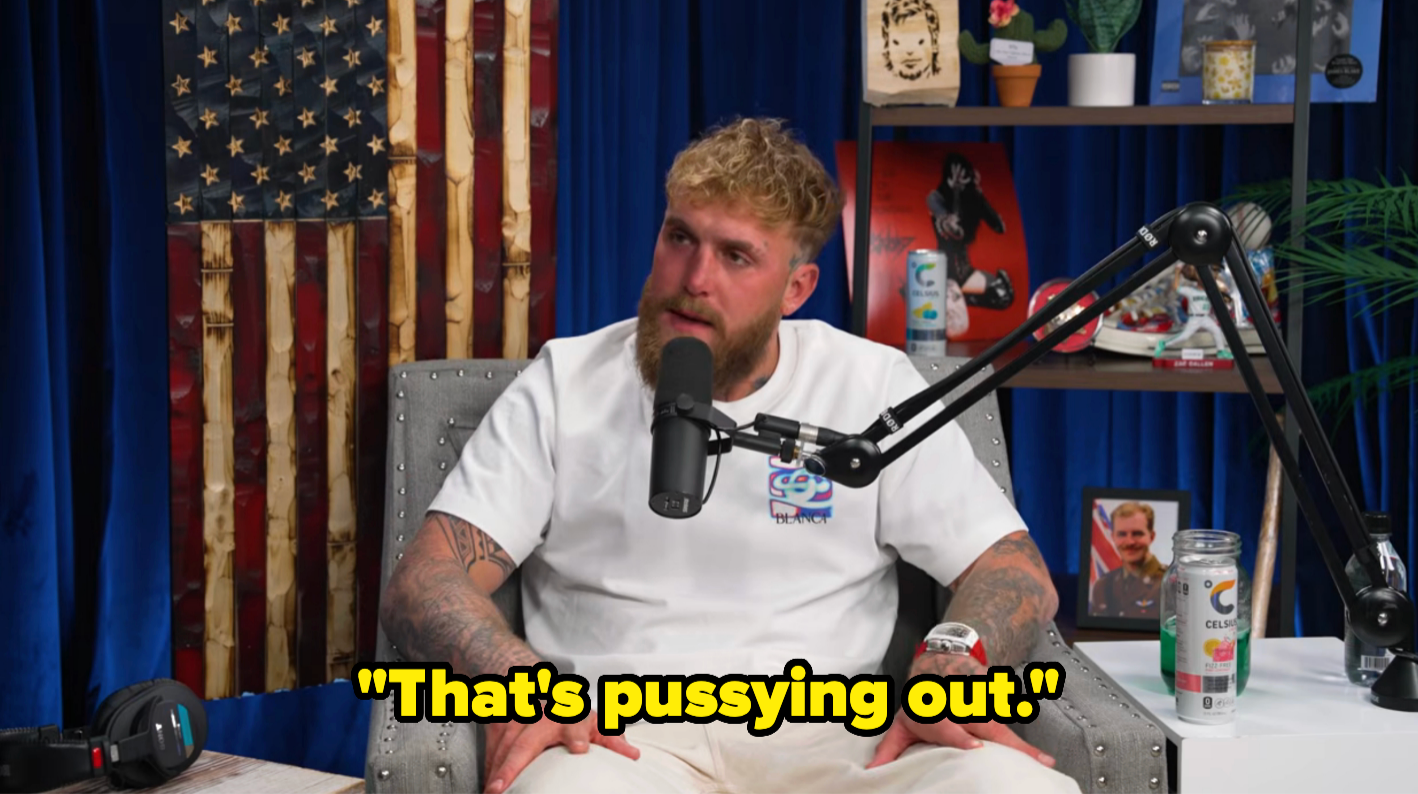 A idiosyncratic   with tattoos is speaking into a microphone connected  a podcast, saying, "That's pussying out."