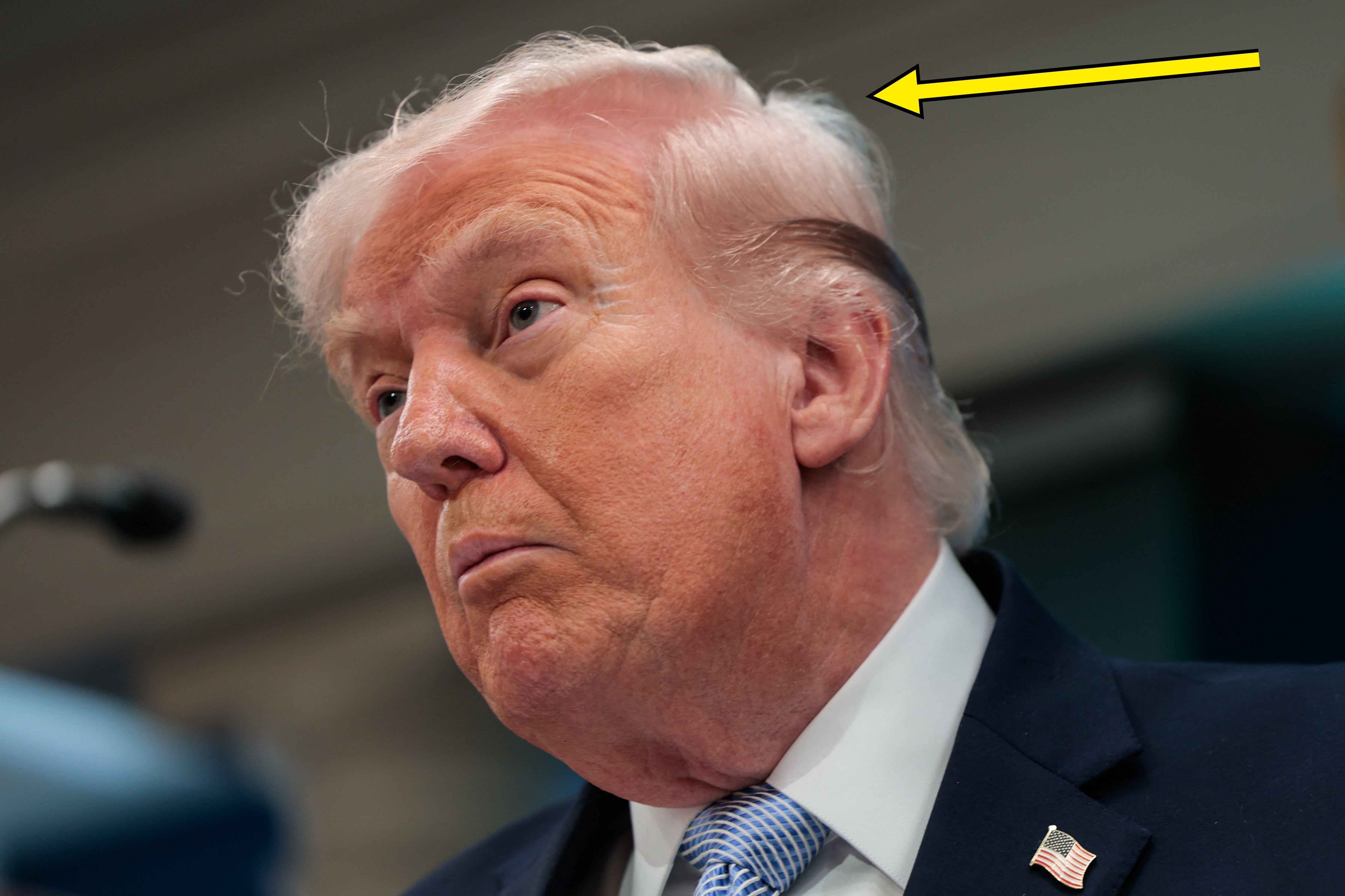 Donald Trump taler ved et podium, en pil peker på det rotete håret hans