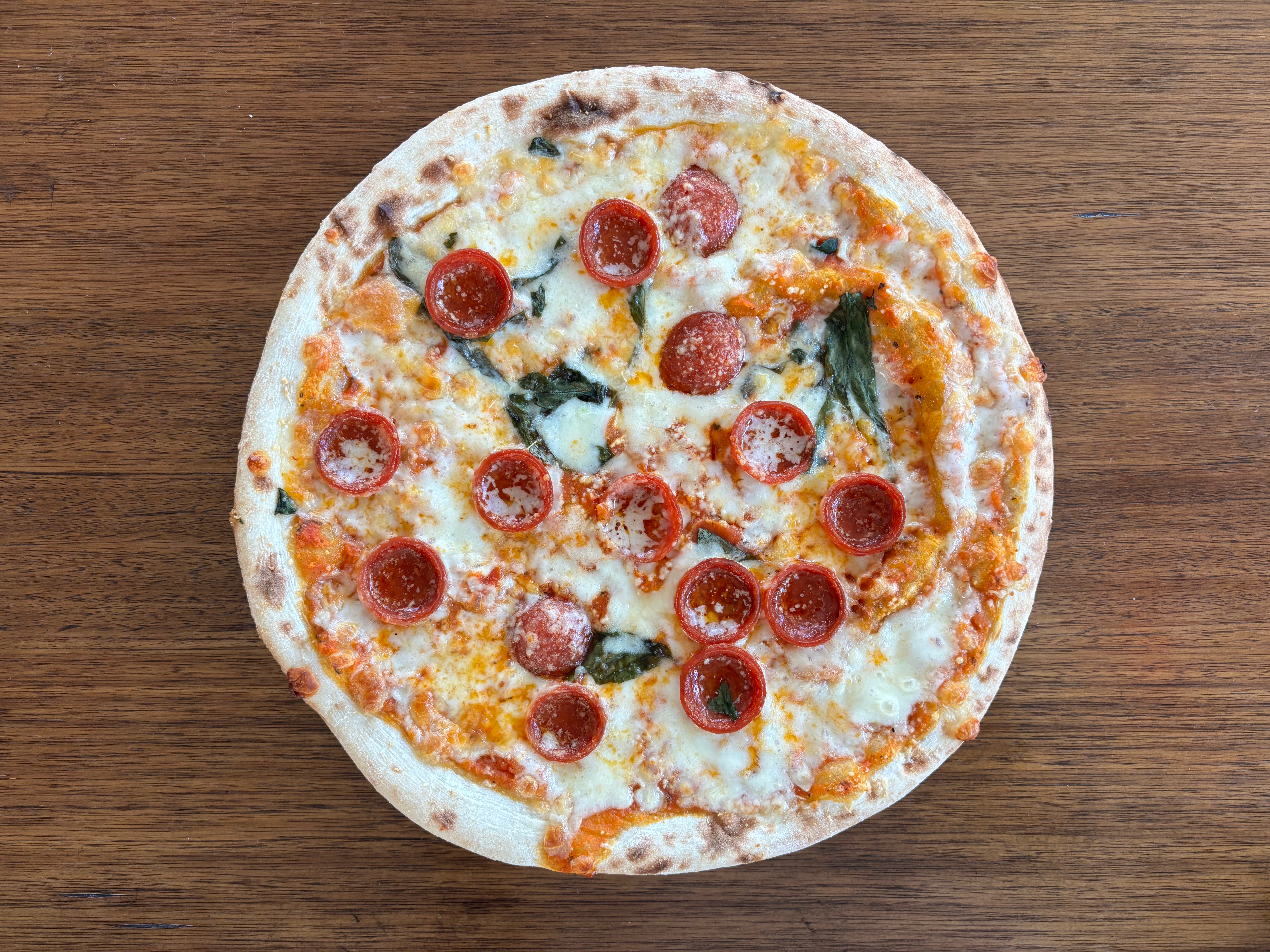 Pepperoni pizza with melted cheese and basil on a wooden table