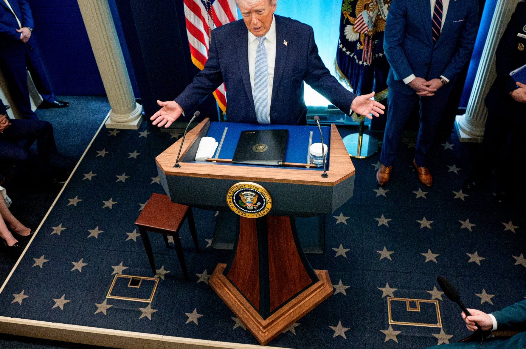 Donald Trump henvender seg til et orienteringsrom fylt med presse og tjenestemenn, stående bak en talerstol med presidentseglet