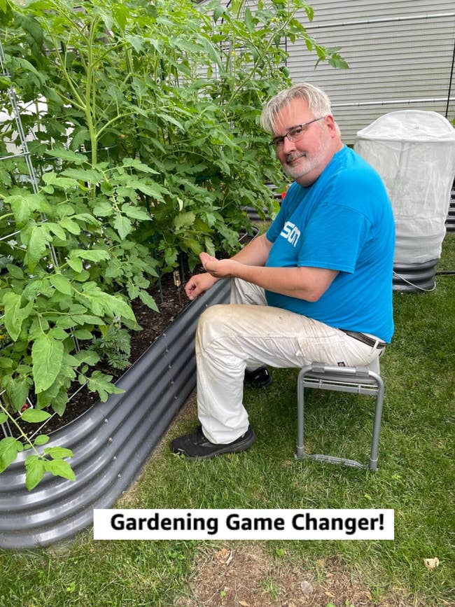 Person successful a bluish garment and achromatic pants sitting connected a stool, gardening adjacent to a raised metallic planter with lush greenish plants