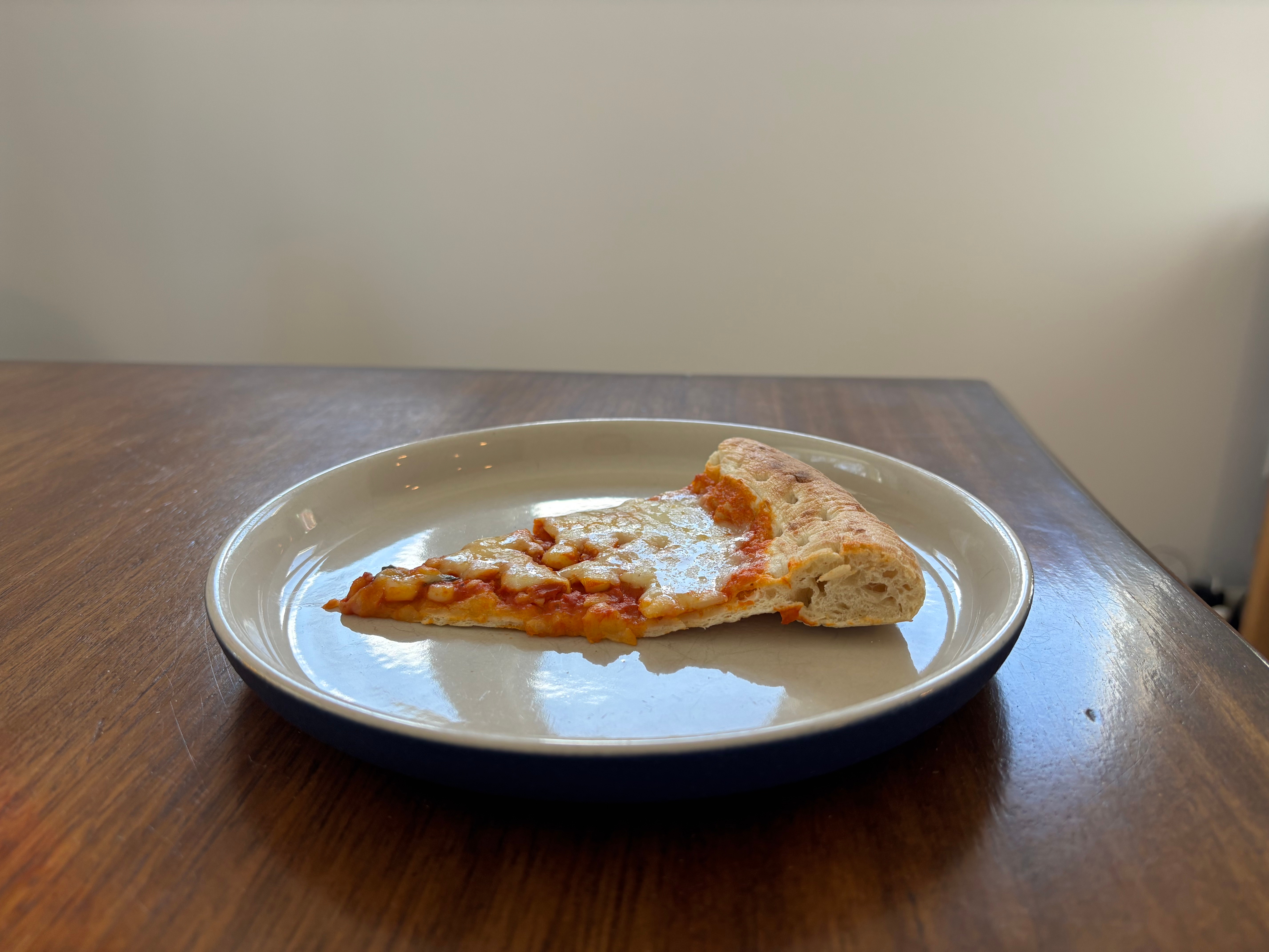 Slice of pizza with tomato sauce and cheese on a plate, resting on a wooden table