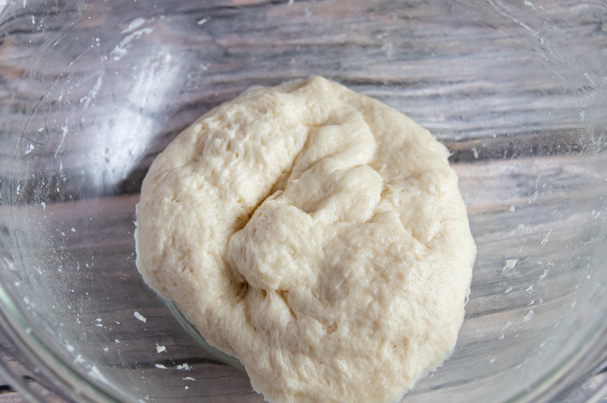 ガラスボウルの中に発酵前のパン生地が置かれている。木製のテーブルの上にボウルがある。