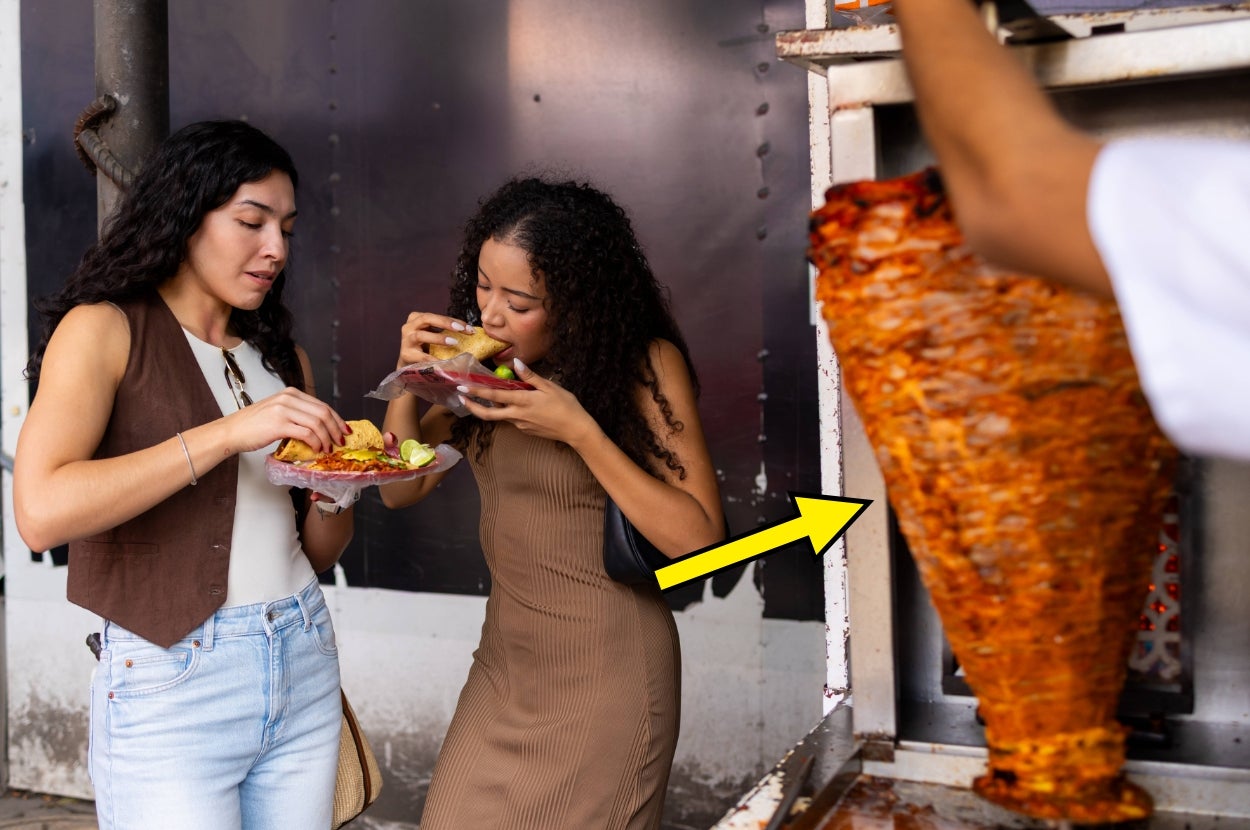 Two people enjoying street food with a large shawarma cone in the background. One is eating a wrap, the other a plate of seasoned meat